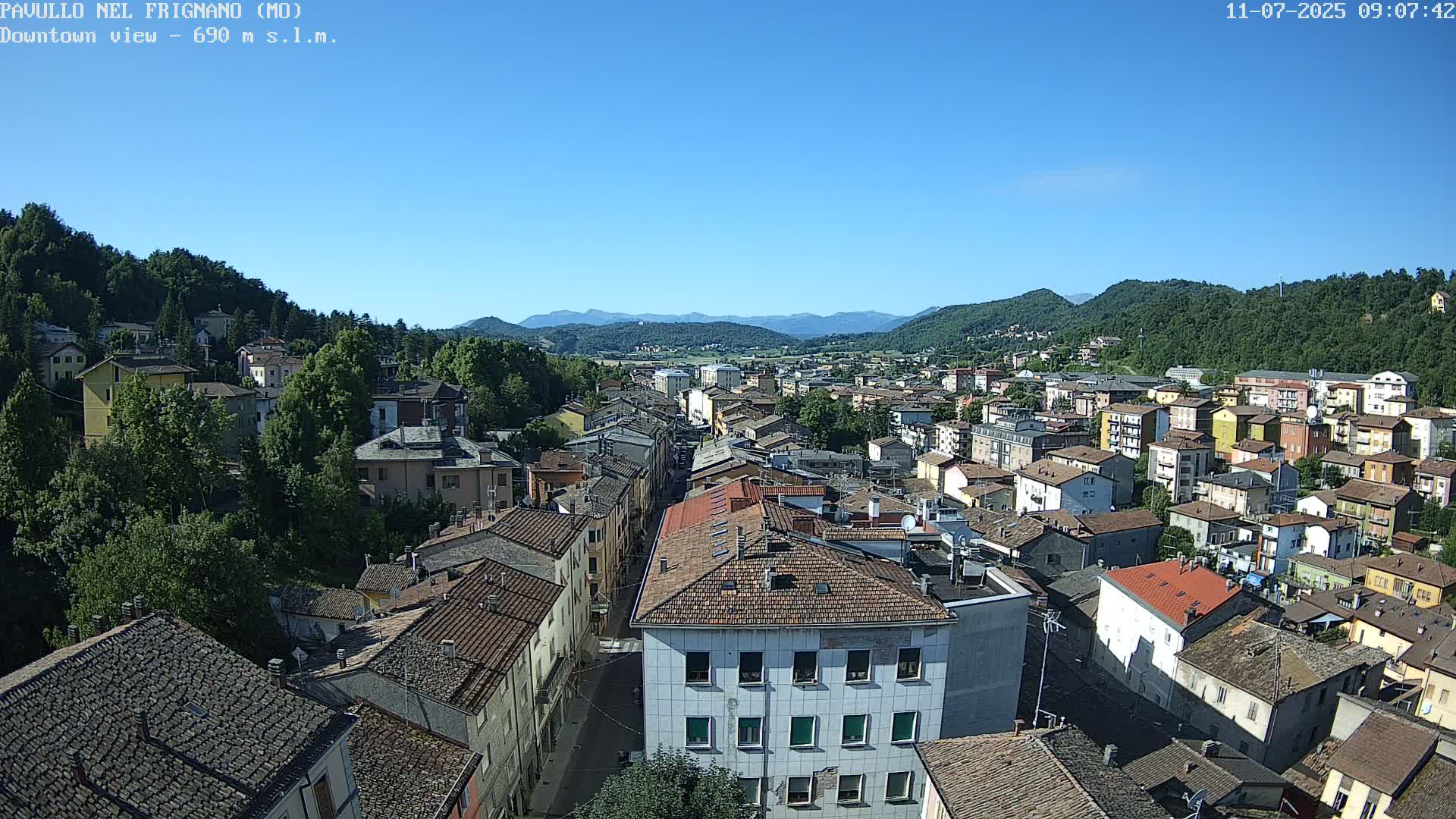 A clear, sunny day view of a dense town nestled in a valley surrounded by hills and mountains.