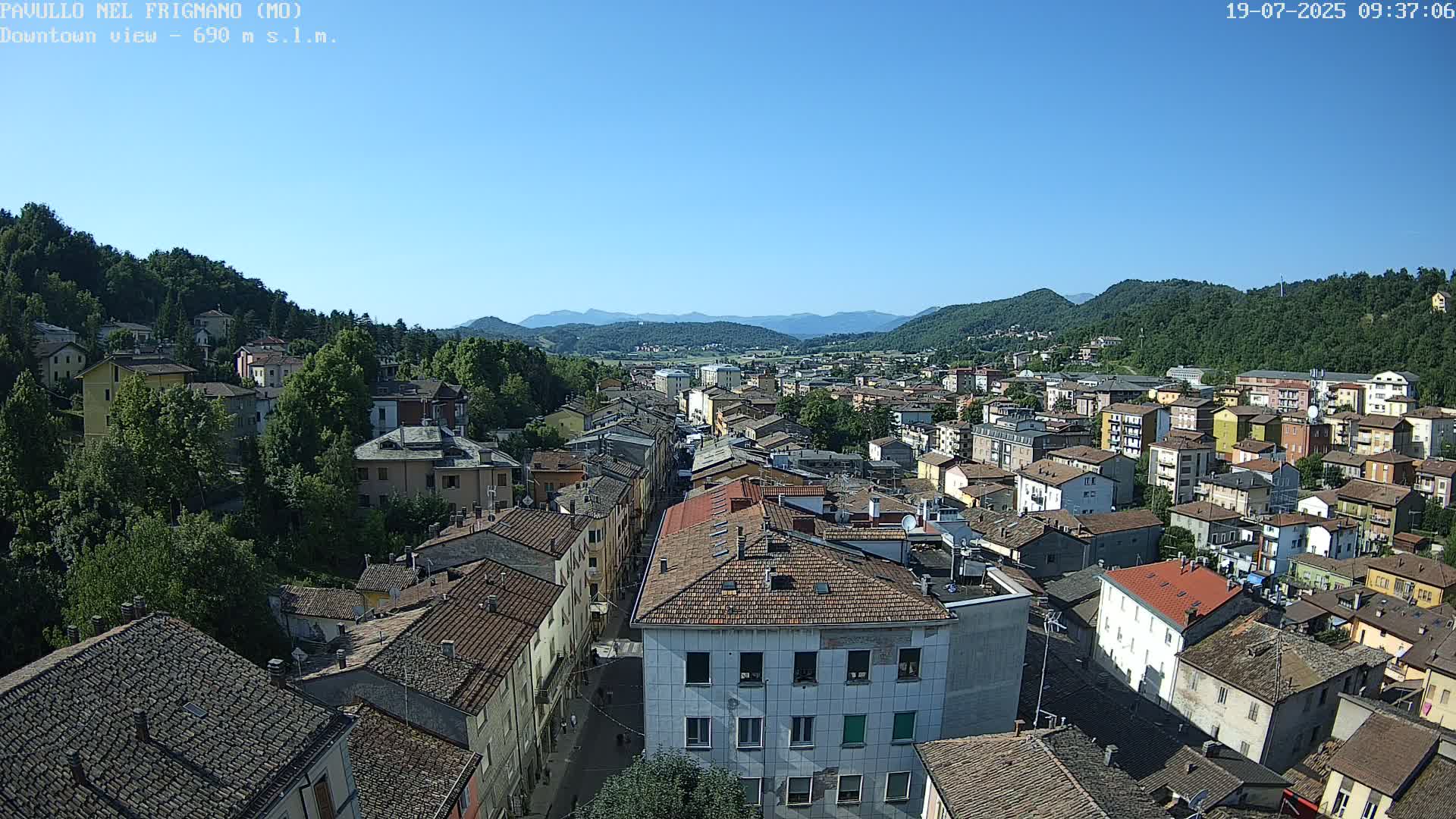 A high-angle view of a town nestled in a valley between mountains on a clear, sunny day.