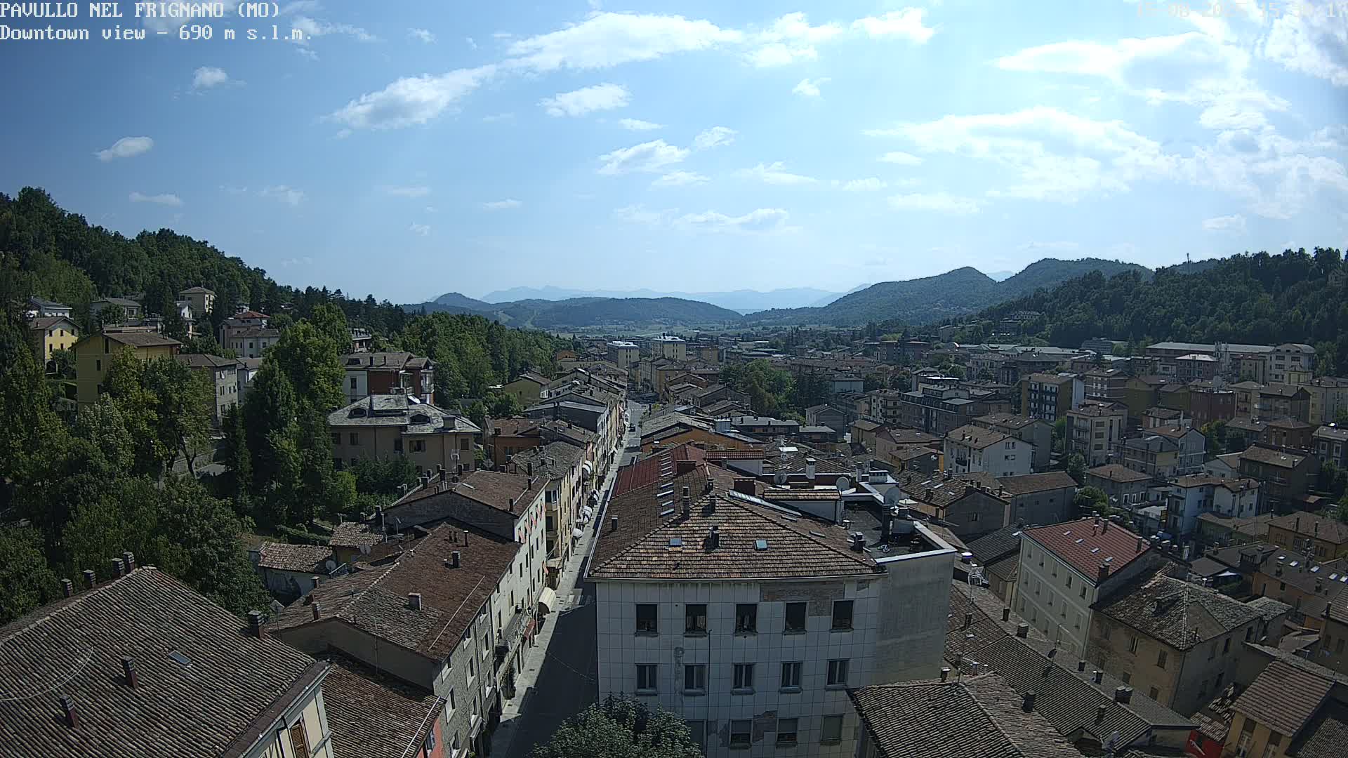 A mostly sunny day reveals a sprawling town nestled in a valley between verdant hills and mountains.