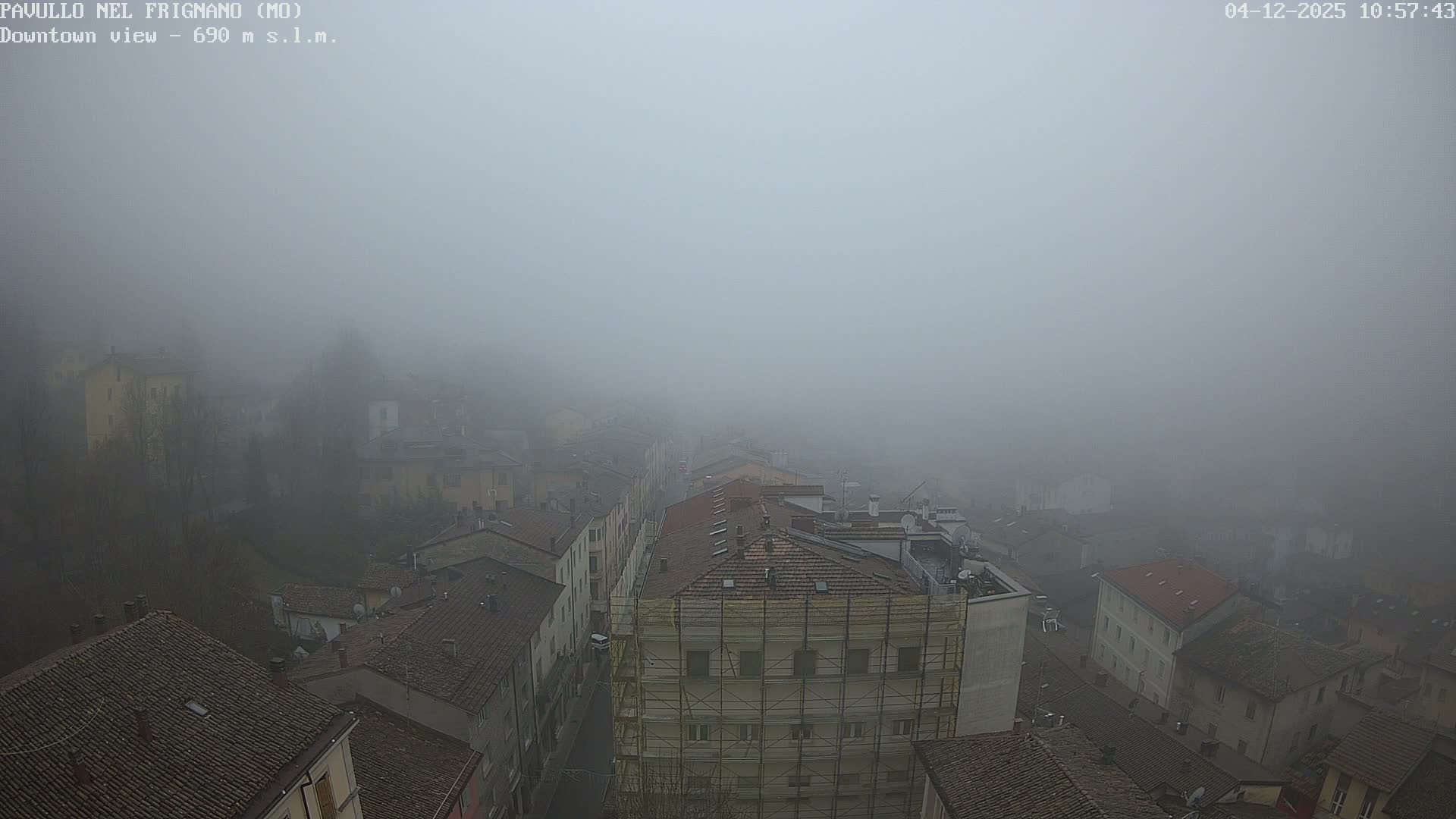 A heavy fog obscures the view of a town from above, revealing densely packed buildings with mostly tiled roofs and a street, with one large building prominently covered in scaffolding.