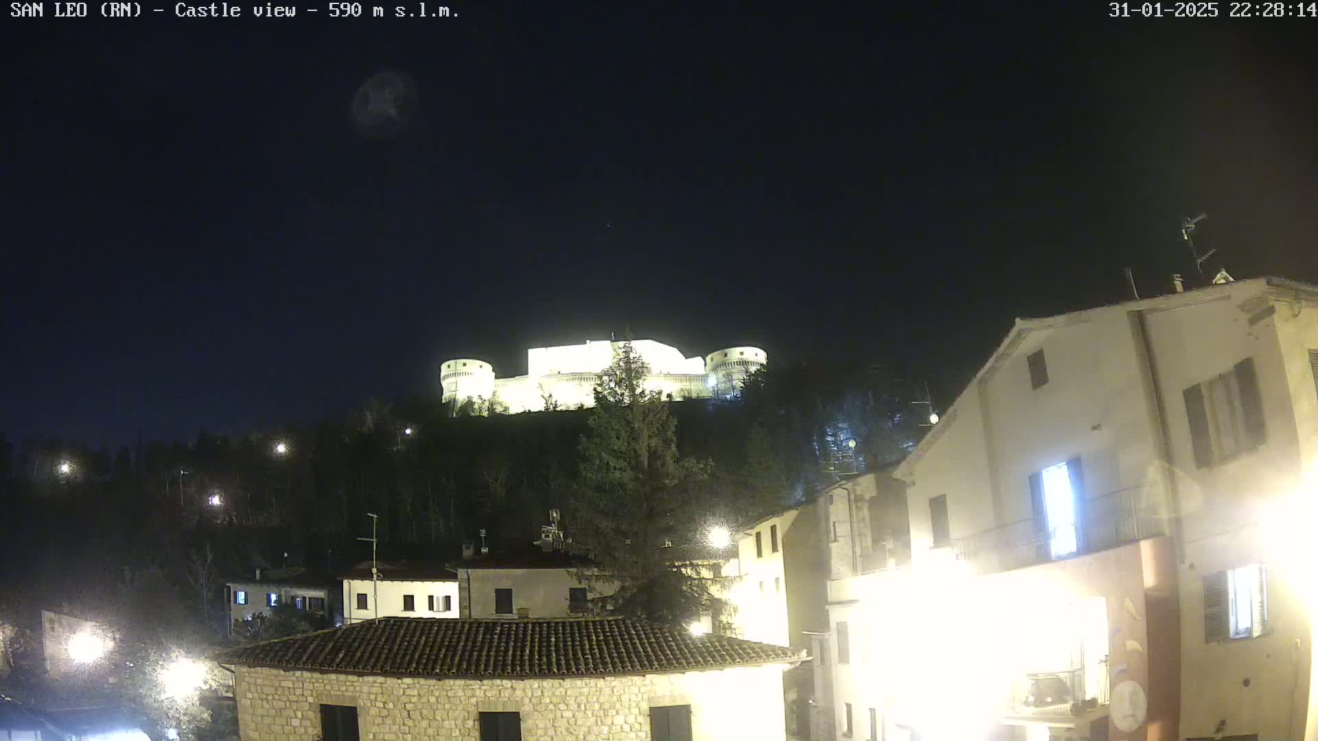 A brightly lit castle sits atop a hill overlooking a small town at night under a clear, dark sky.