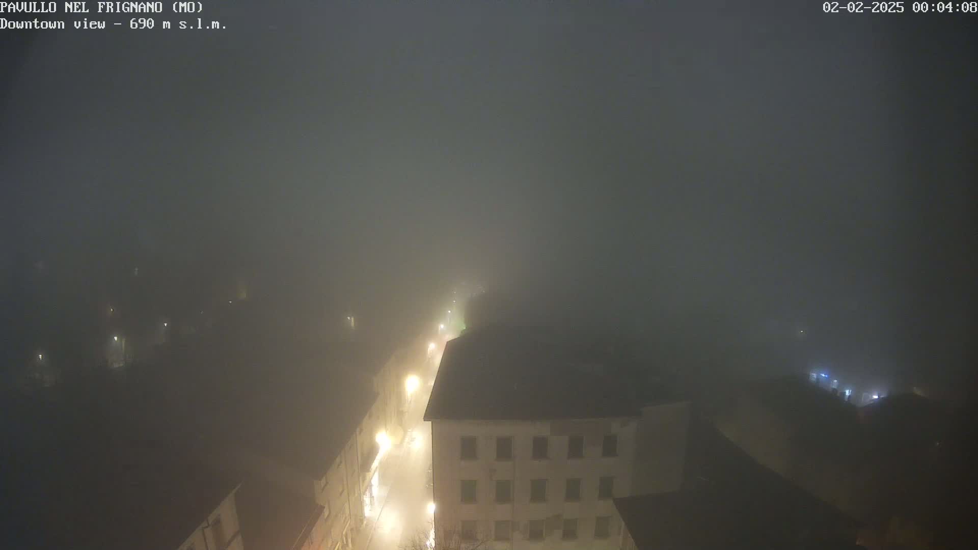 A nighttime, foggy view of a town shows dimly lit buildings and streets.