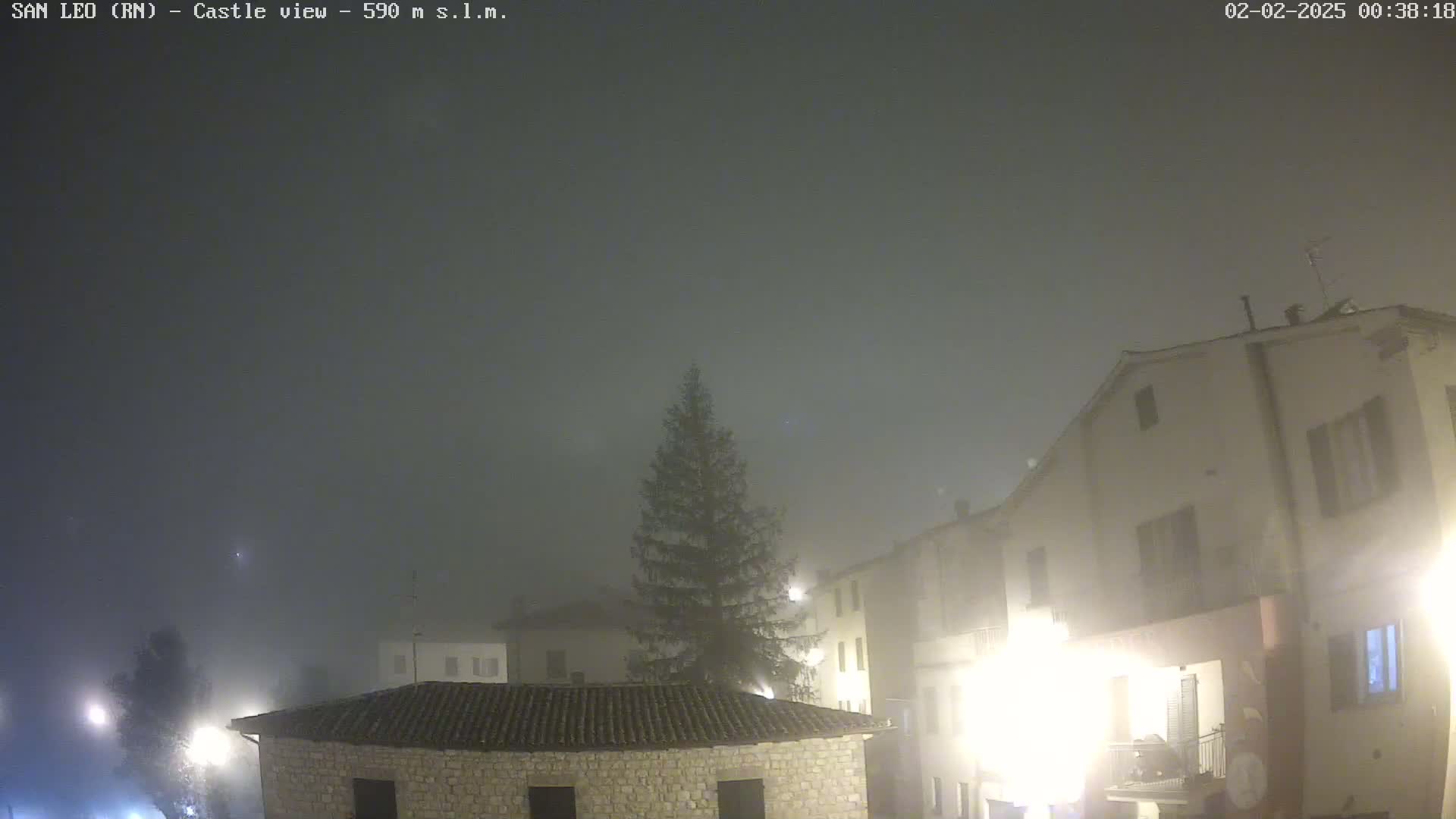 A foggy night scene shows several stone buildings illuminated by streetlights.