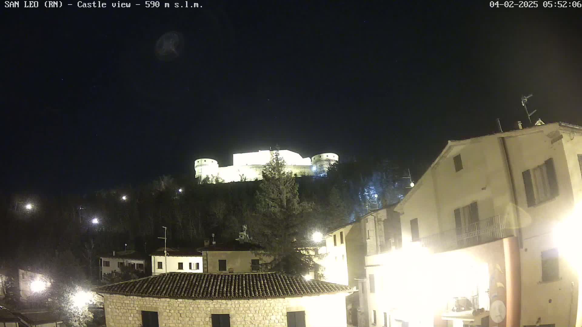 A brightly lit castle sits atop a hill overlooking a town at night under a clear, dark sky.