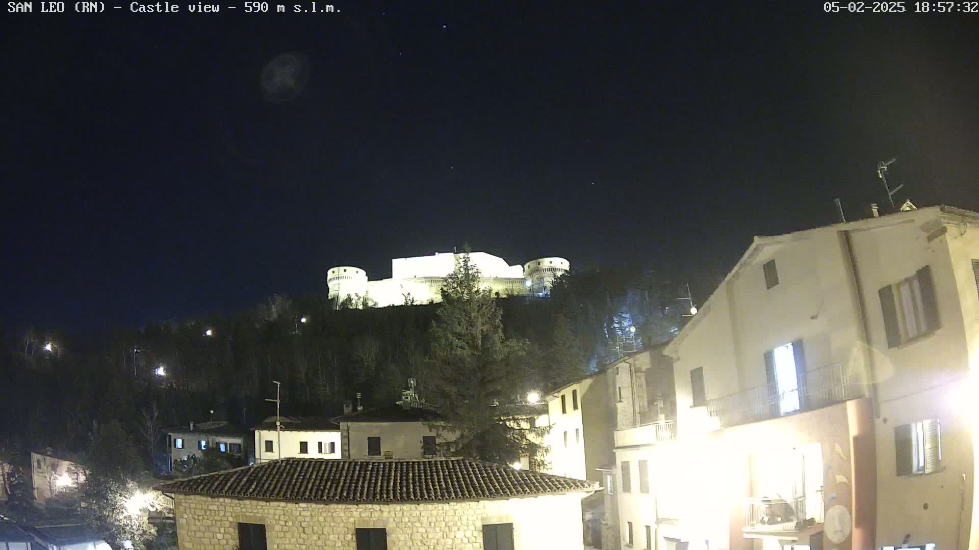 A well-lit castle sits atop a hill at night, overlooking a town with buildings illuminated under a clear, dark sky.