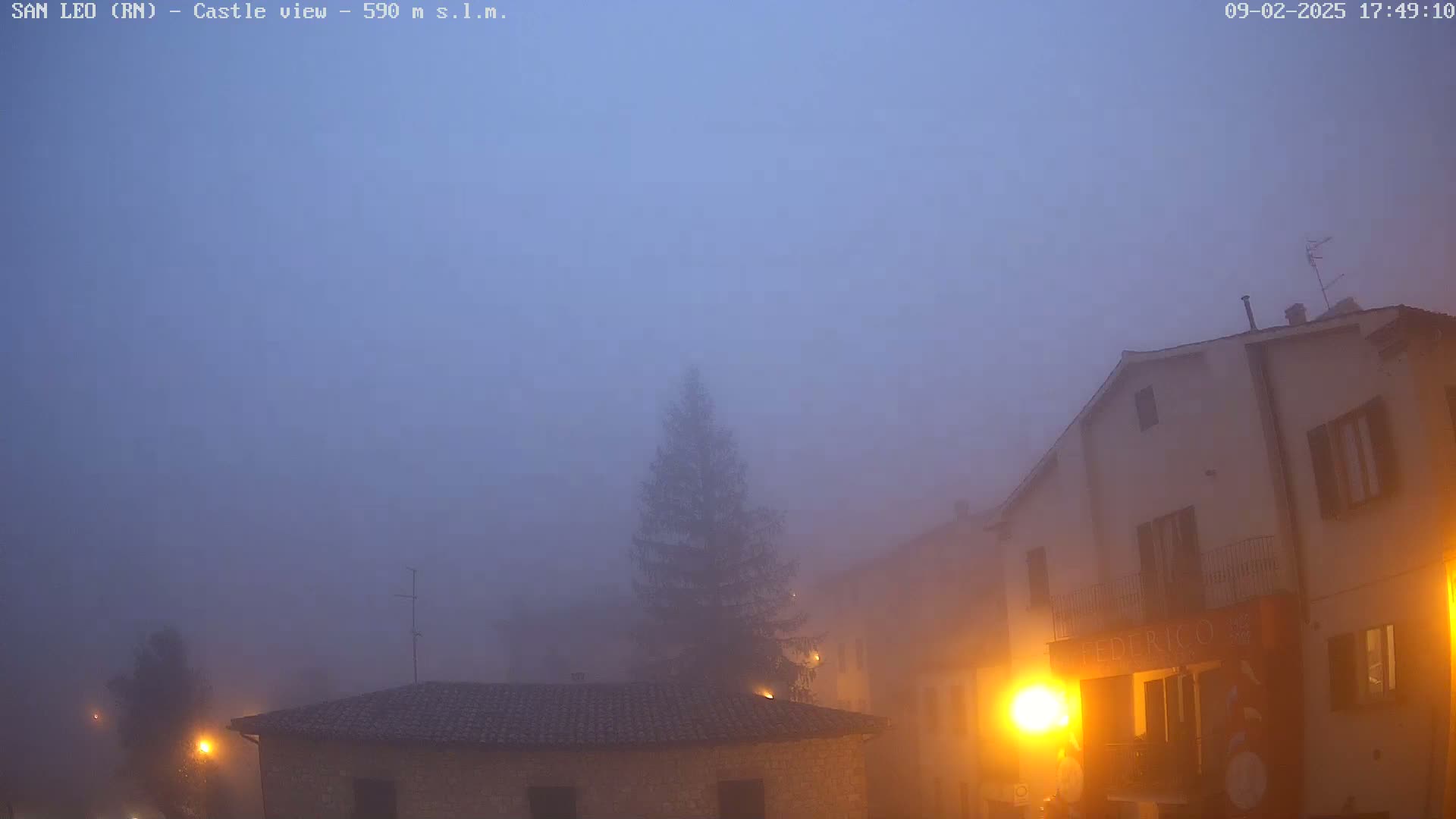 A foggy, twilight scene shows several stone buildings and a lone evergreen tree in a small town.