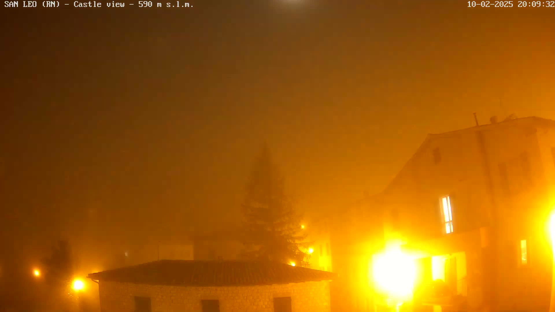 A thick fog obscures a nighttime view of buildings with illuminated windows, lit by streetlights.