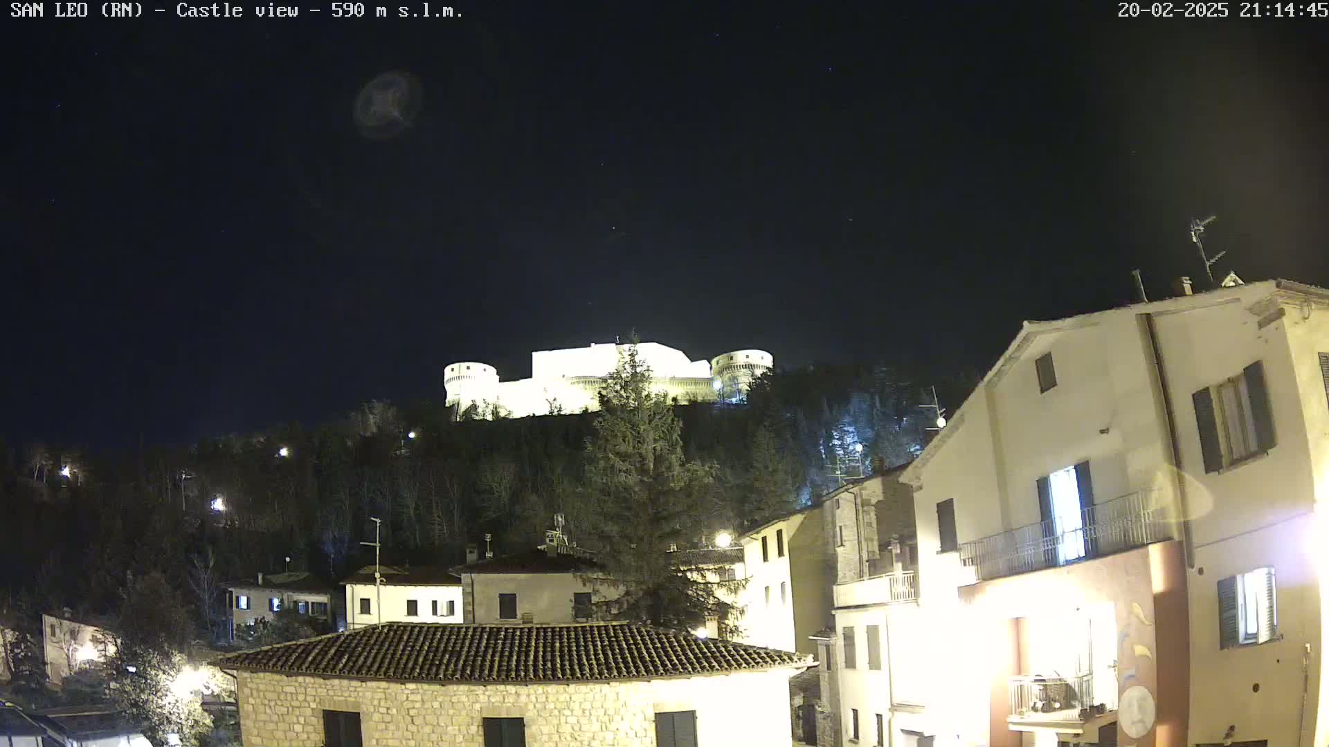 A brightly lit castle sits atop a hill overlooking a town at night under a clear, dark sky.