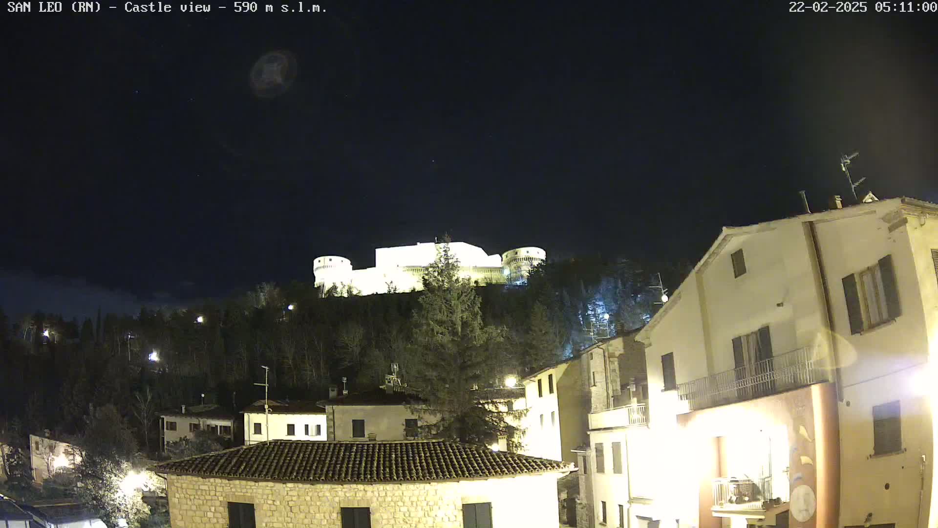 A nighttime view of a castle perched atop a hill overlooking a town, under a clear, dark sky.