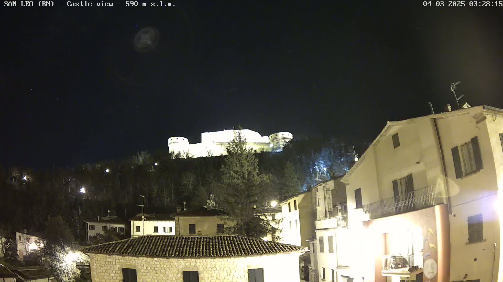 A brightly lit castle sits atop a hill overlooking a town at night under a clear, starry sky.