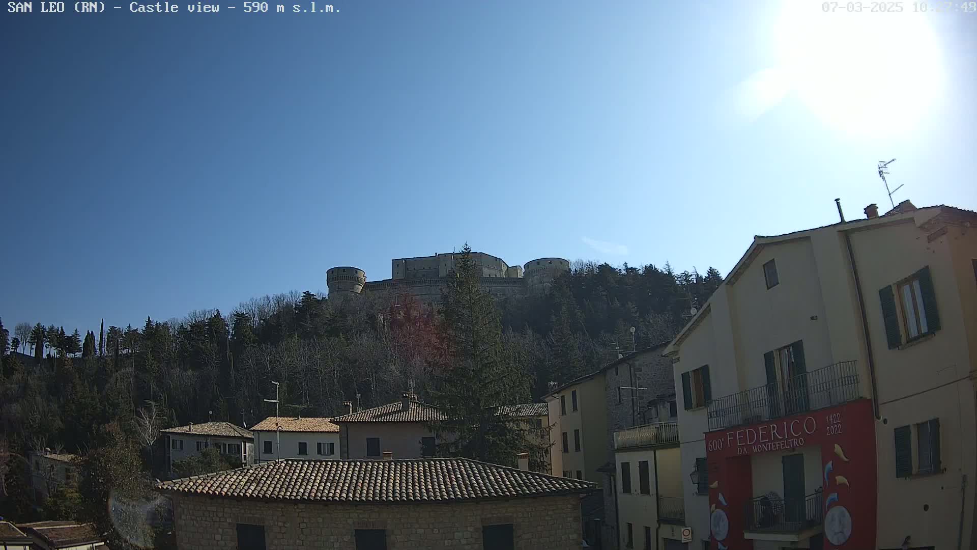 A hilltop castle is visible in the distance, under a clear blue sky, overlooking a village of stone buildings.