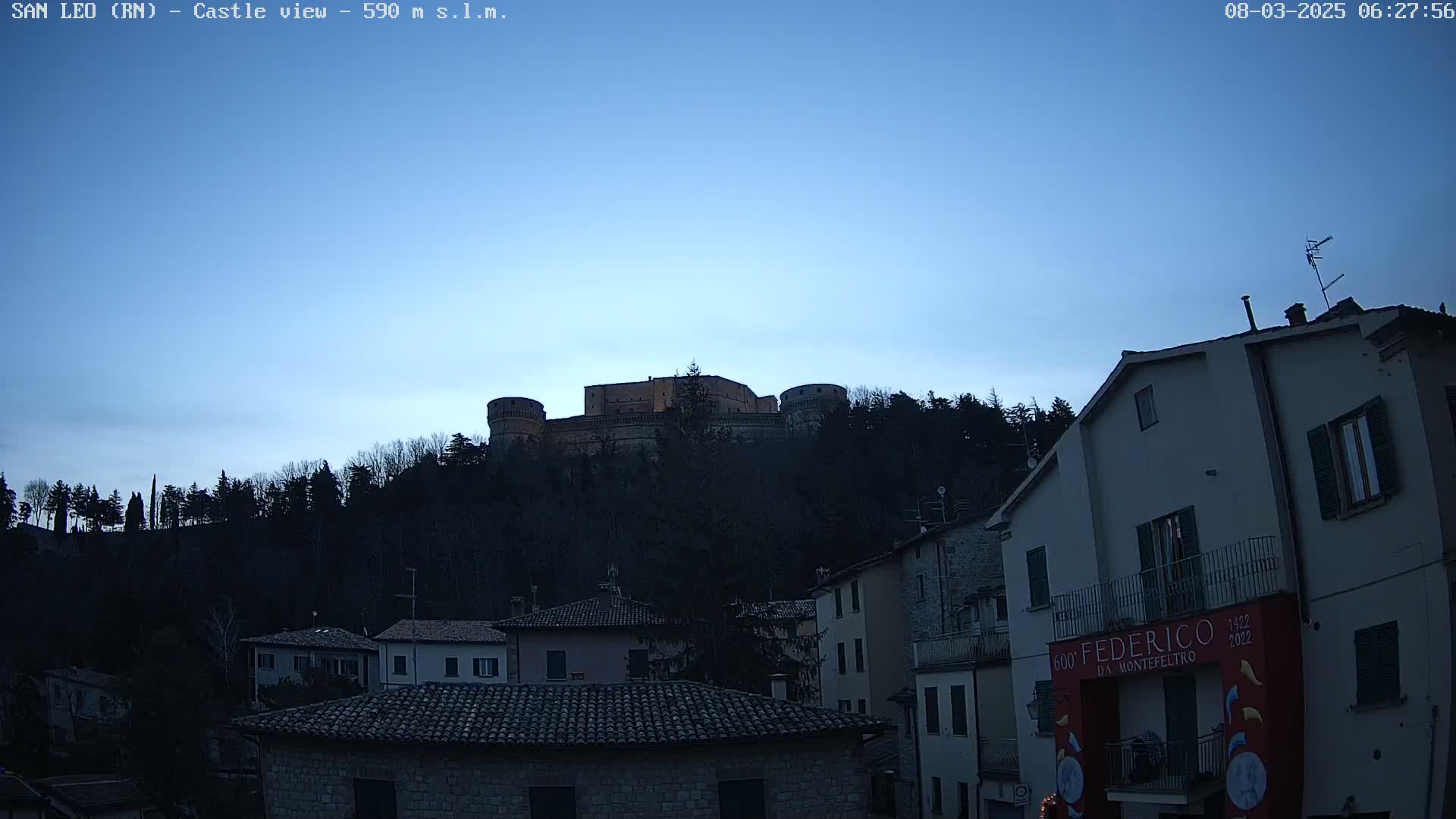 A castle sits atop a hill overlooking a town at twilight under a clear blue sky.