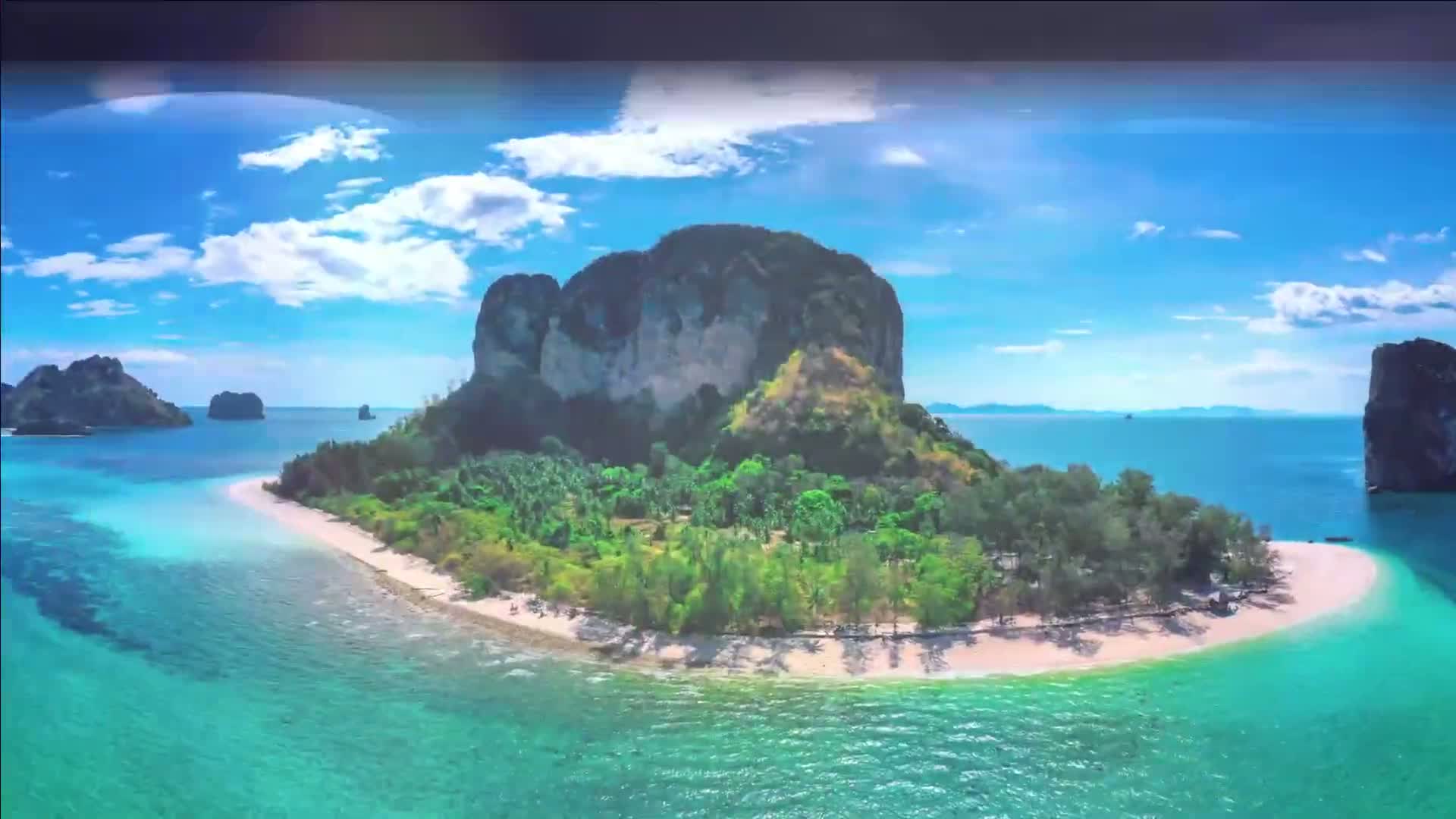 An aerial view shows a tropical island with a white sand beach, lush green vegetation, and a large, imposing rock formation under a bright, sunny sky with scattered clouds.
