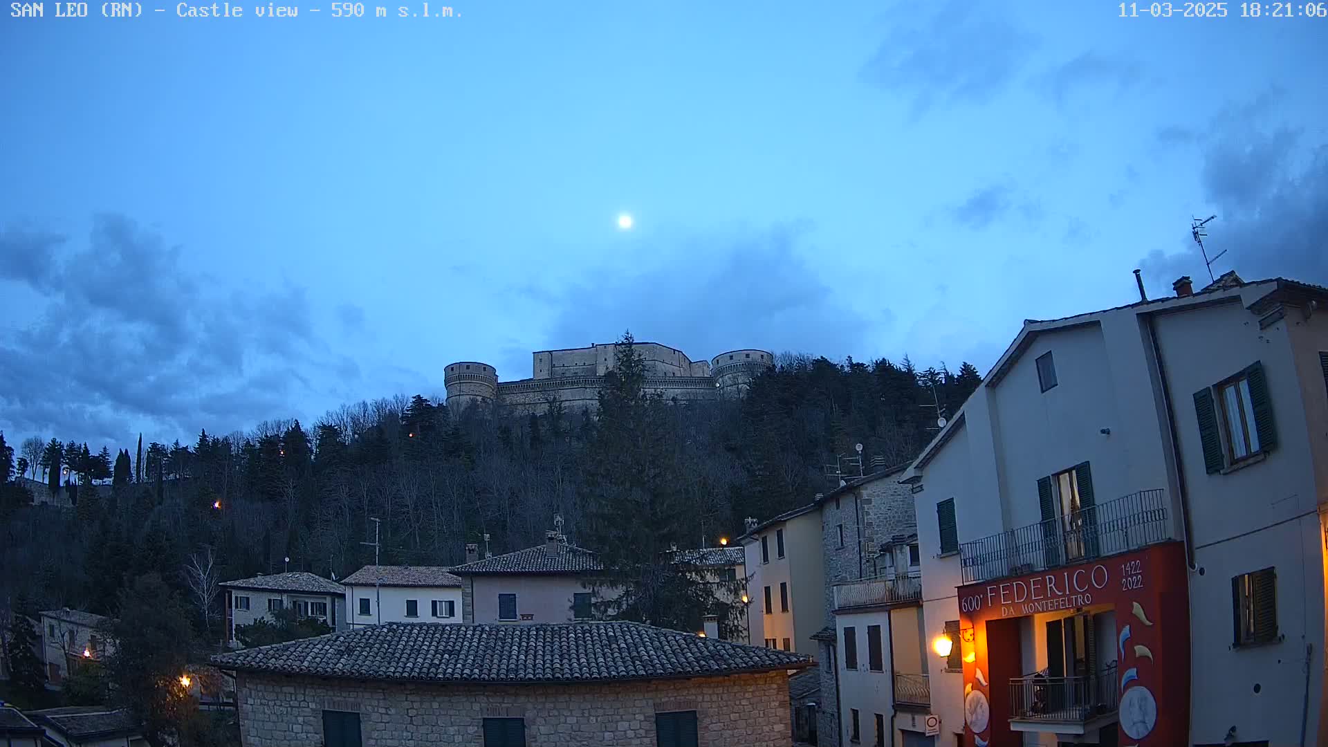 A hilltop castle is visible above a town at dusk under a partly cloudy sky.