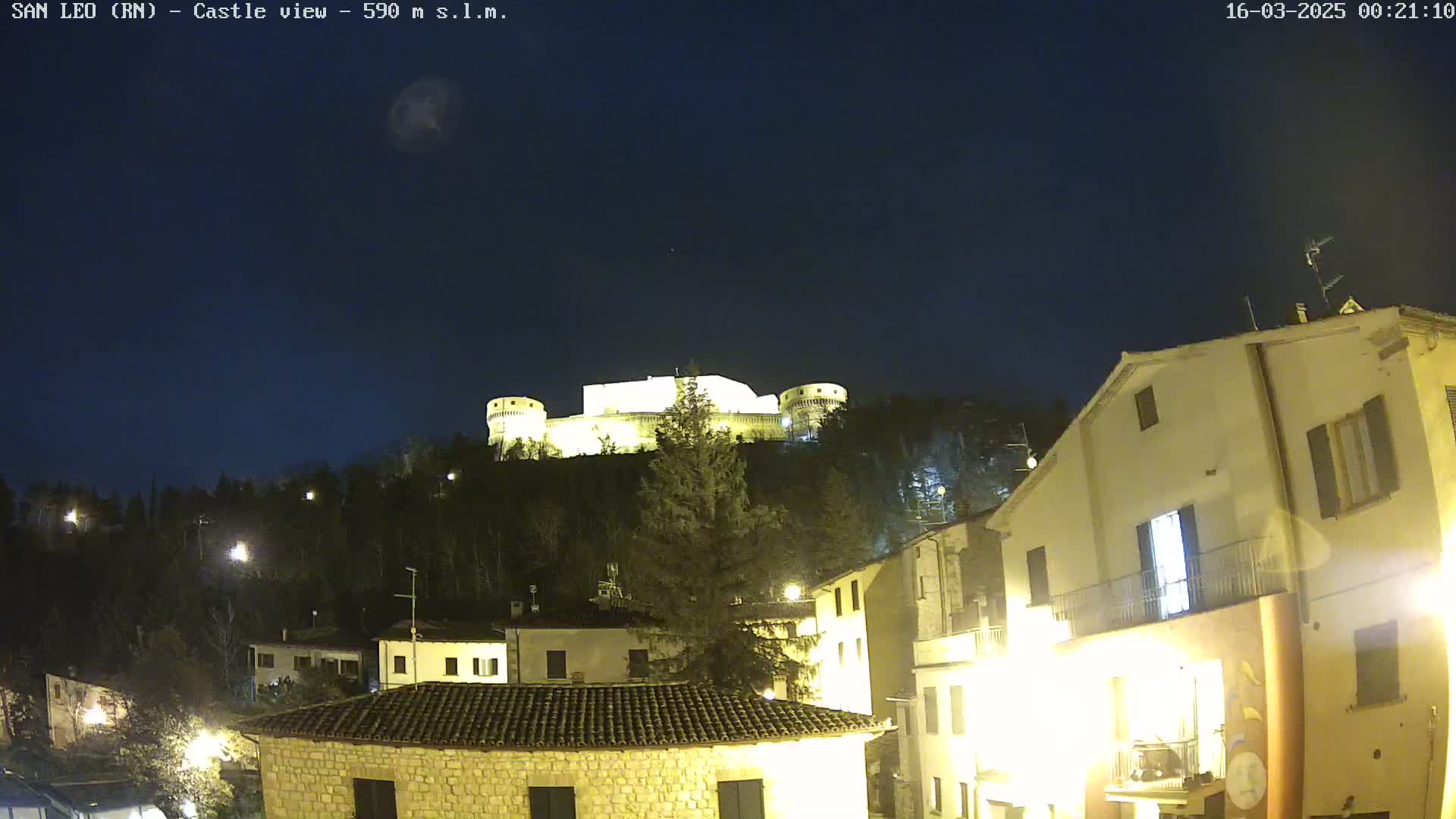 A hilltop castle is illuminated at night, overlooking a town of low buildings under a clear, dark sky.