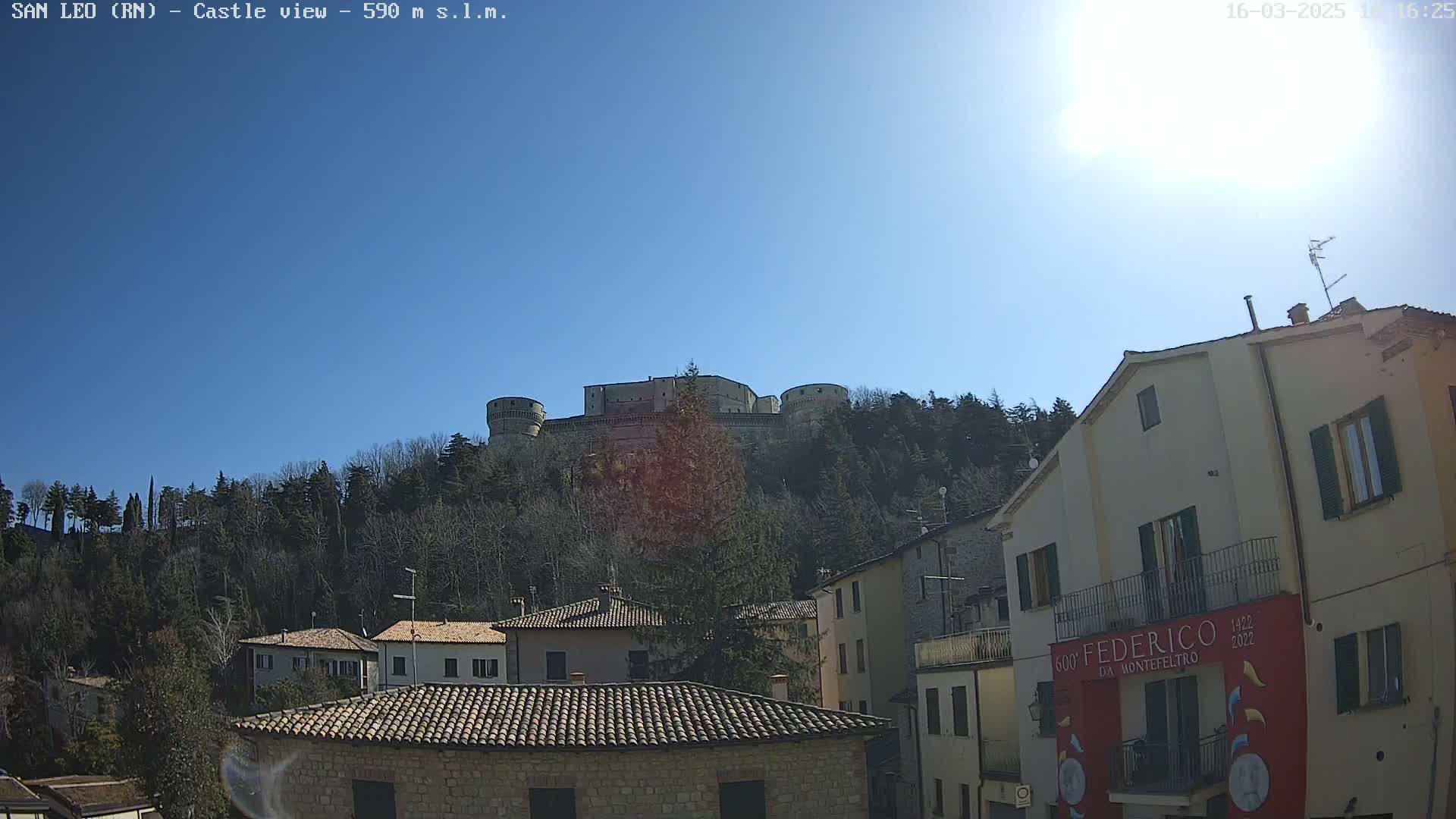A hilltop castle is visible in the distance under a clear, sunny sky, overlooking a village of stone buildings.