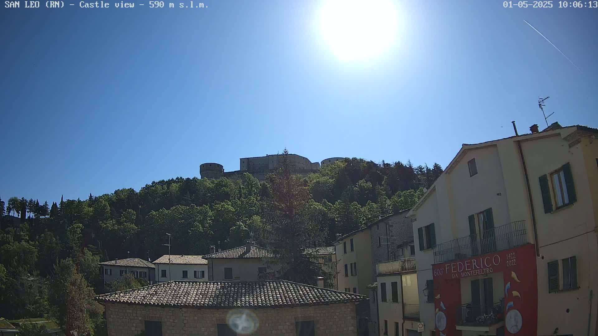 A hilltop castle is visible above a sunlit town of buildings under a clear blue sky.