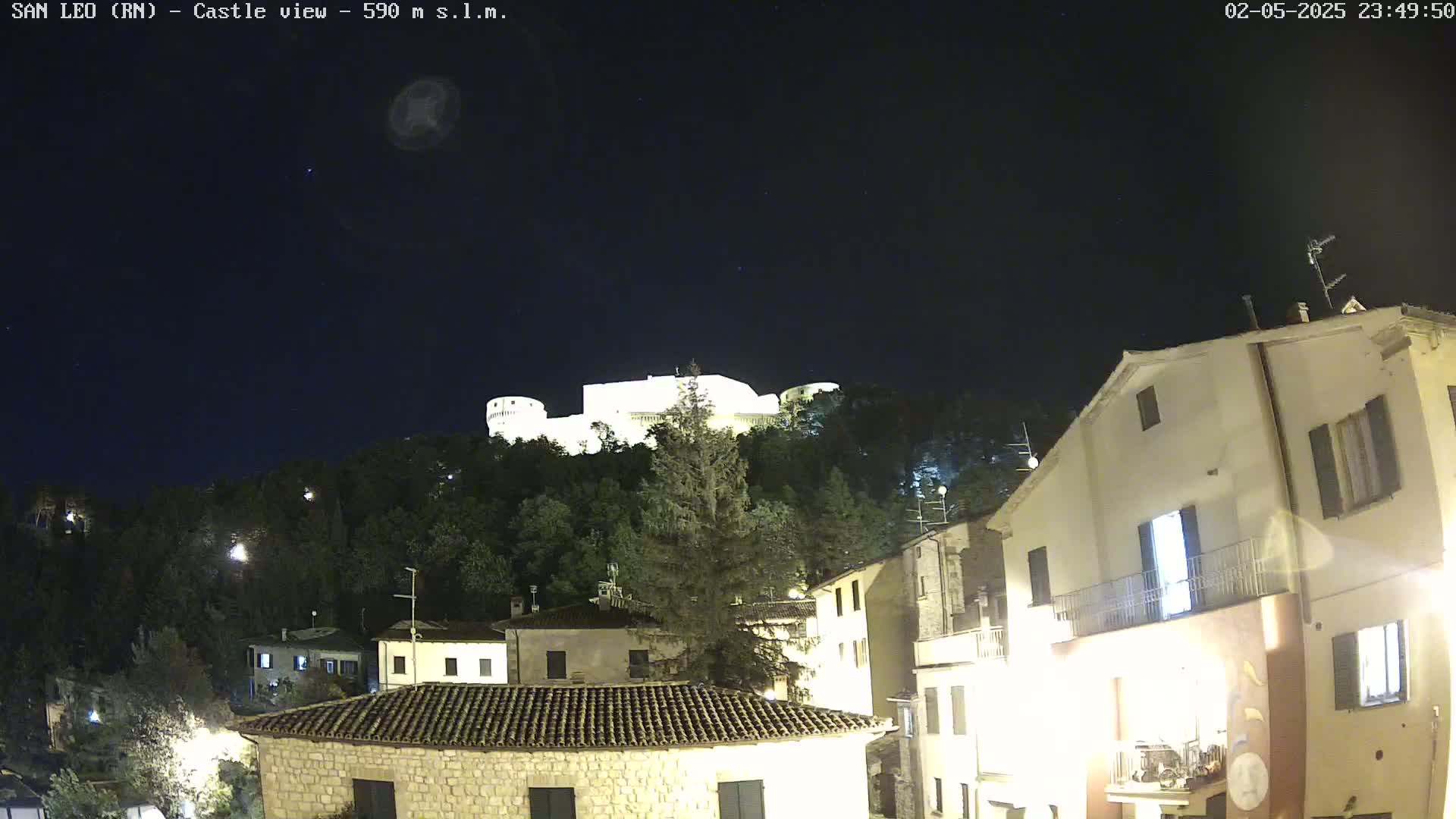 A nighttime view of a castle perched atop a hill overlooking a village of buildings under a clear, starry sky.