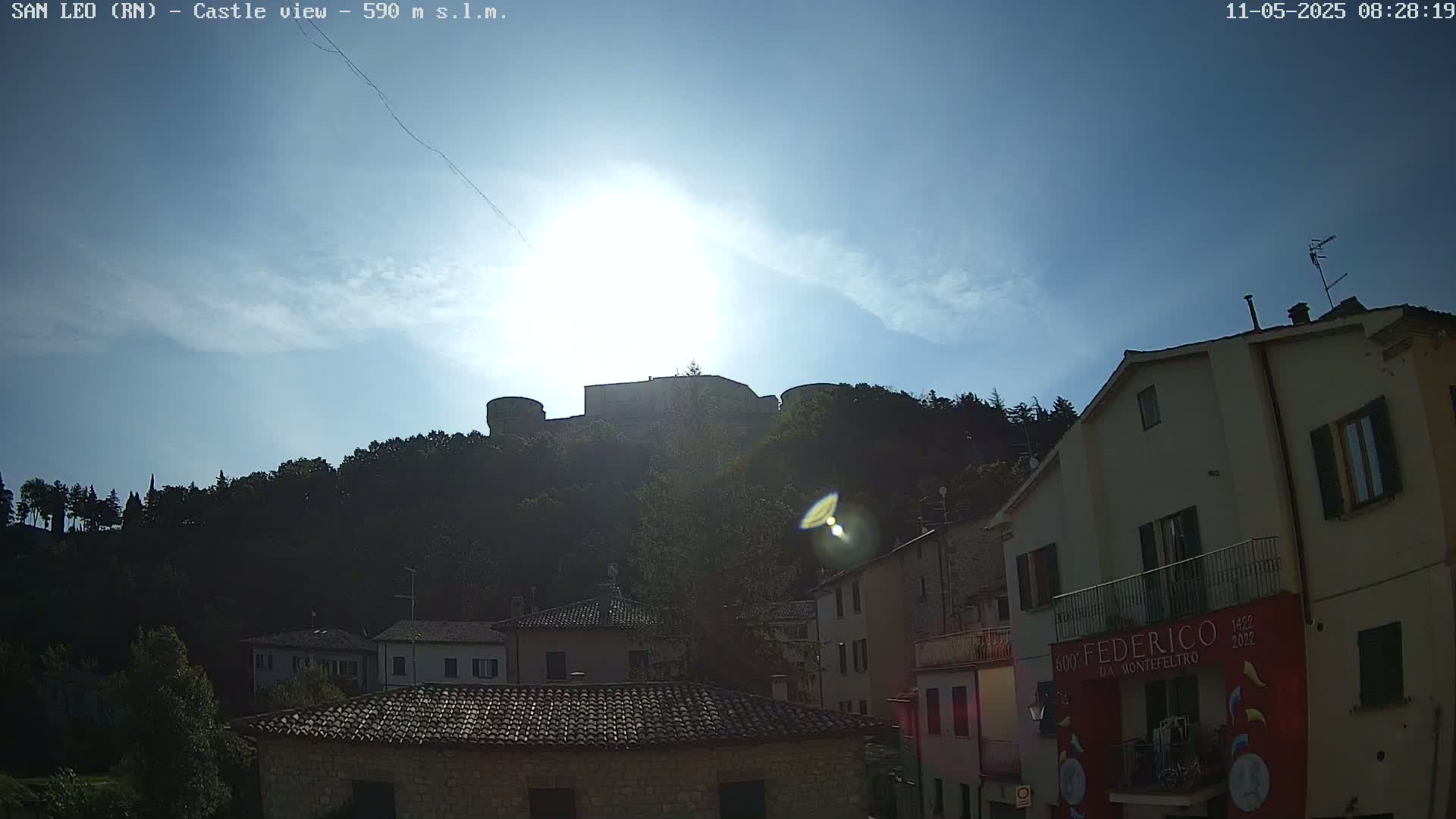 A hilltop castle is visible in the distance under a mostly sunny sky, overlooking a collection of buildings in a town.