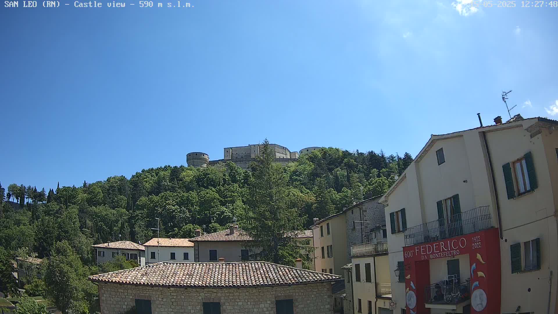 A hilltop castle overlooks a village of stone buildings under a clear blue sky.