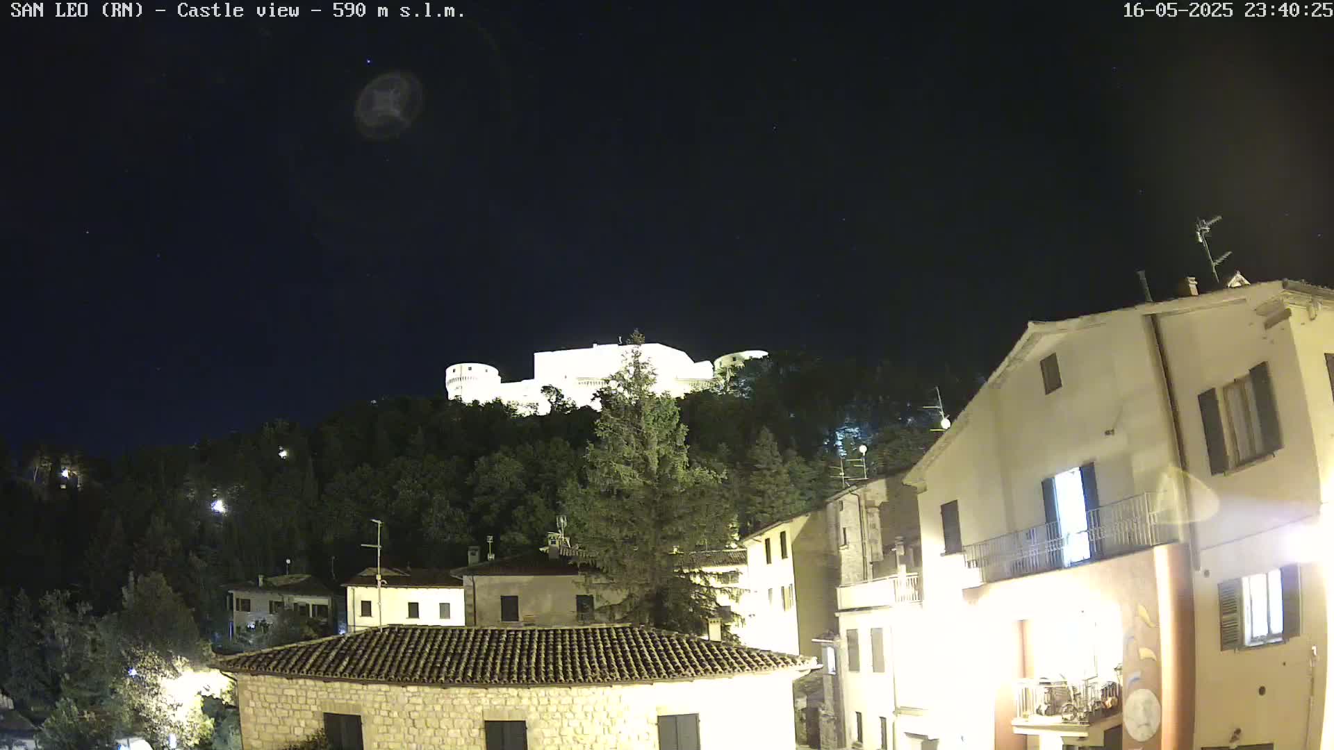 A nighttime view of a castle perched atop a hill overlooking a village, under a clear, starry sky.