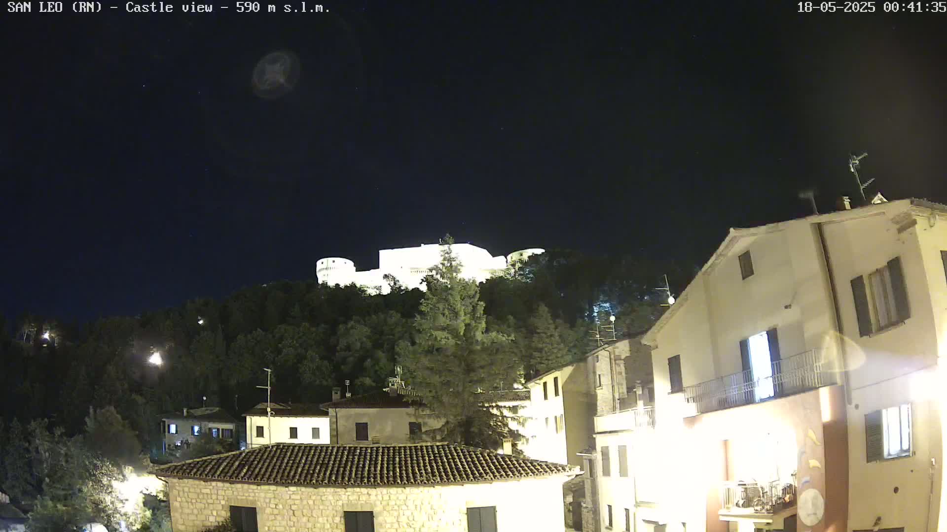 A nighttime view of a castle atop a hill overlooking a village with clear skies.
