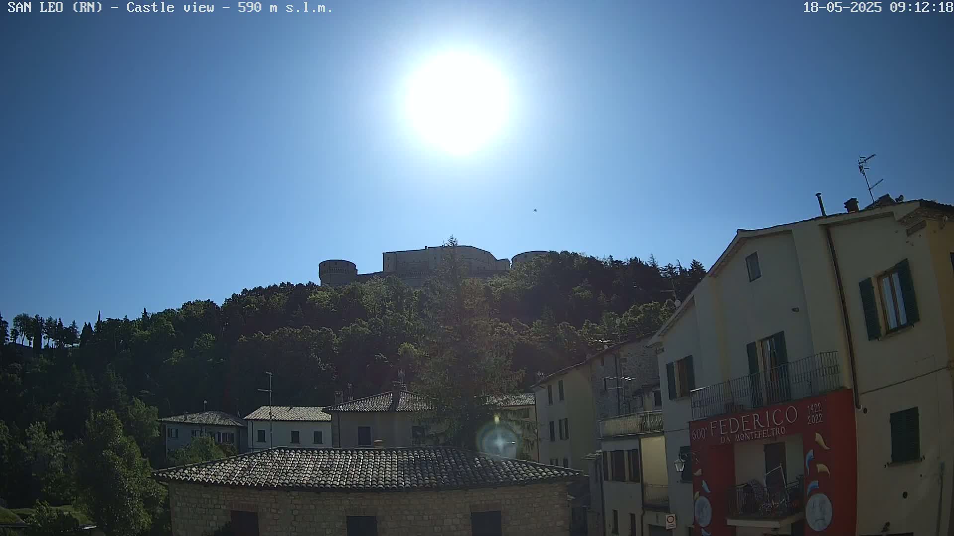 A hilltop castle is visible in the distance above a village of stone buildings under a bright, sunny sky.
