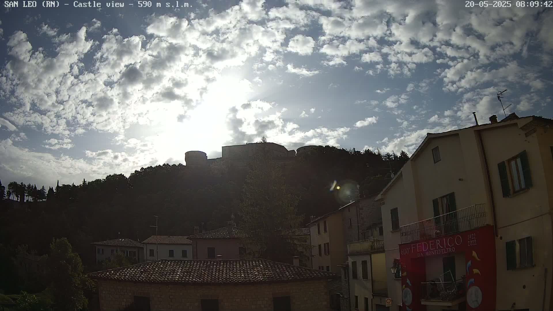 A partly sunny sky with scattered clouds overlooks a hilltop castle and a town of low buildings.