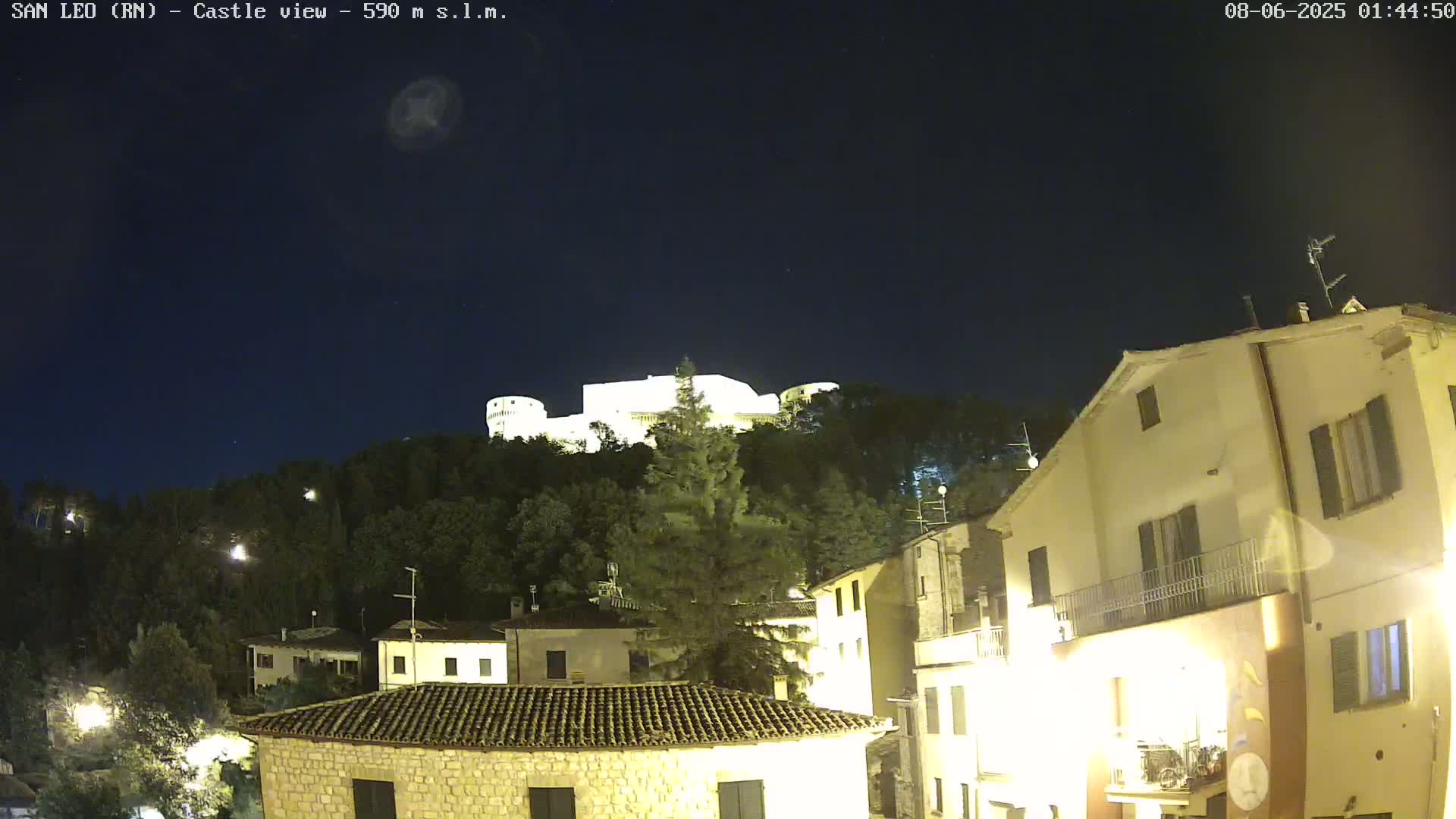 A brightly lit castle sits atop a hill overlooking a town at night under a clear, dark sky.