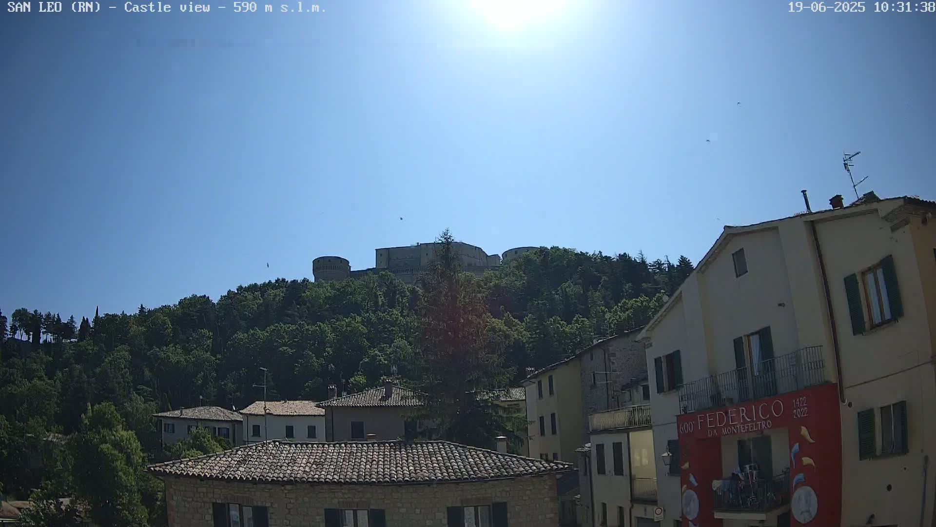 A hilltop castle is visible in the distance above a town of low stone buildings under a bright, sunny sky.