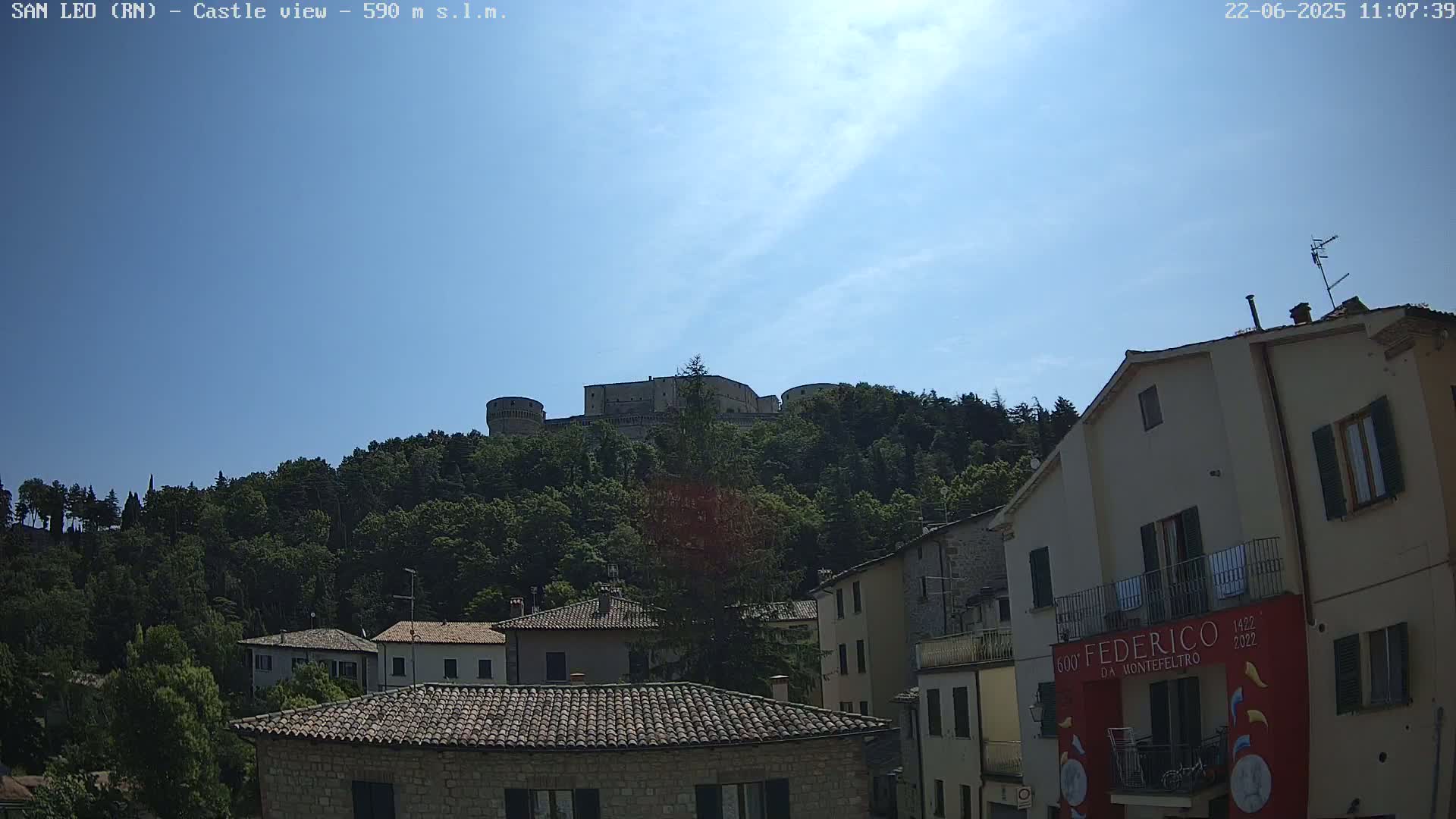 A hilltop castle is visible above a village of stone buildings under a clear blue sky.