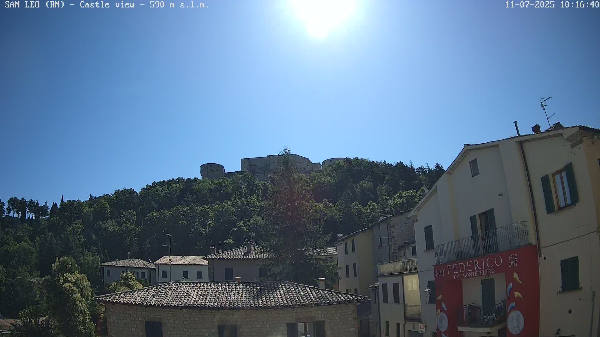 A hilltop castle is visible above a row of buildings under a bright, sunny sky.