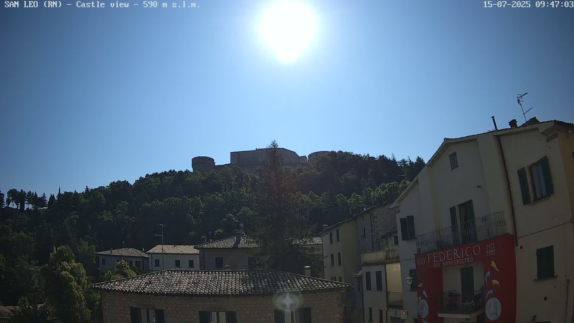 A hilltop castle is visible in the distance above a town of stone buildings under a bright, sunny sky.