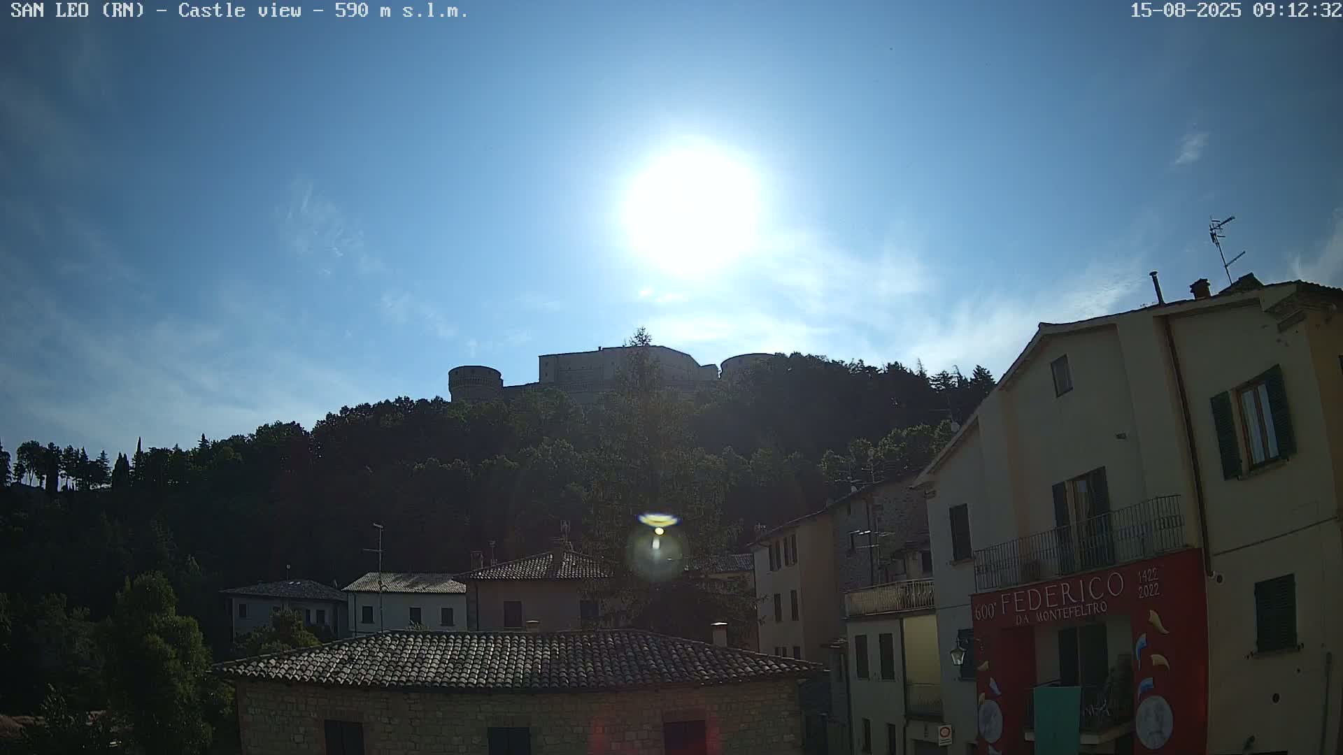 A hilltop castle is visible in the distance under a bright, sunny sky, overlooking a collection of buildings with terracotta roofs.