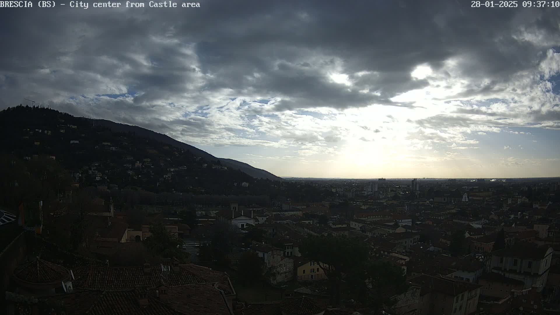 A partly cloudy sky overlooks a city nestled in a valley, with a mountain visible in the background.