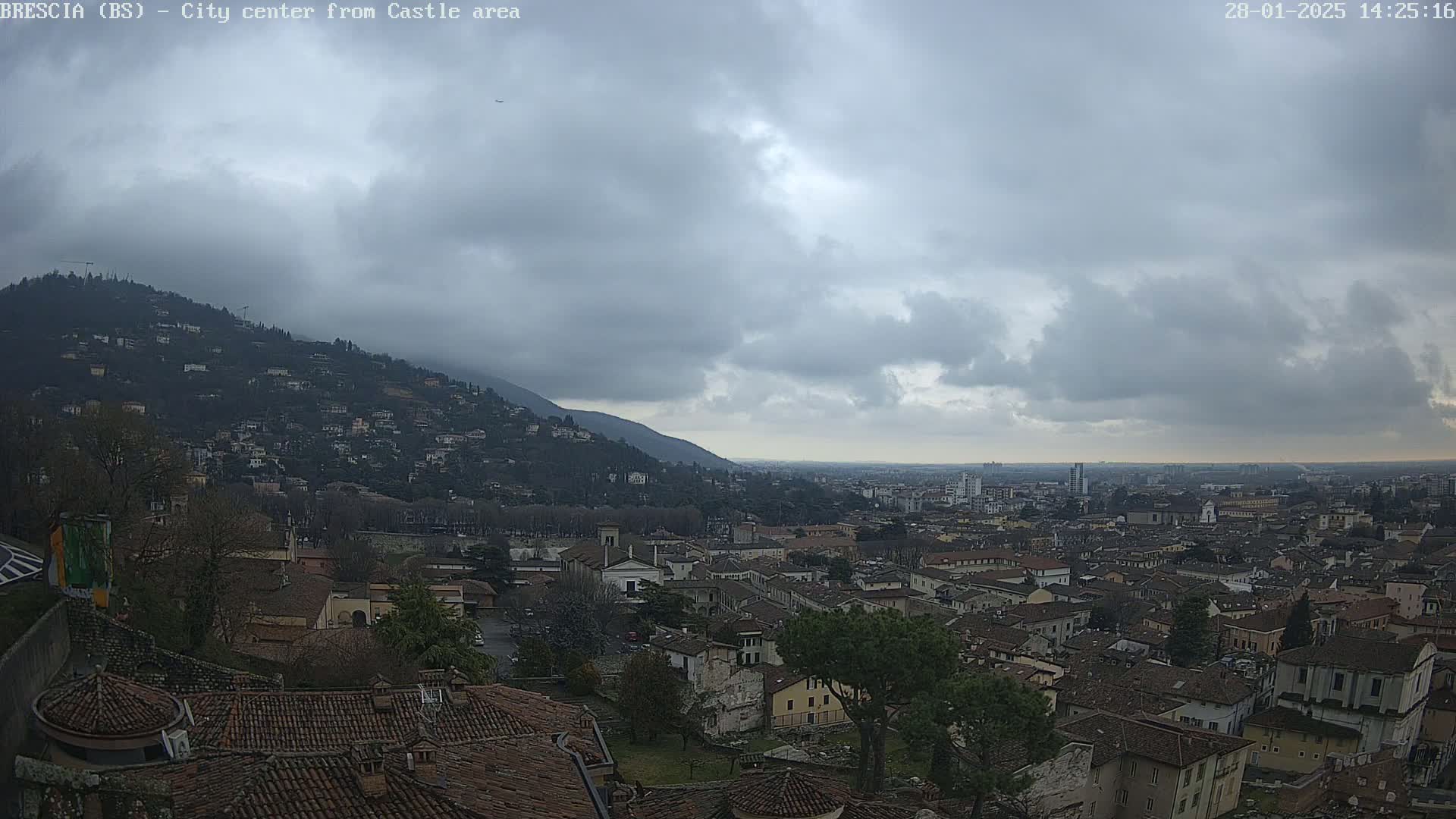 A sprawling city with red-tiled roofs nestles beneath a hill, all under a cloudy sky.