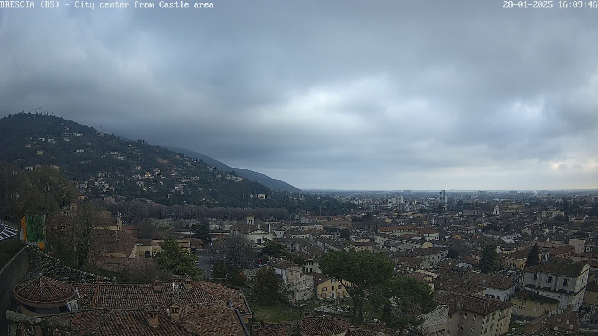 A sprawling city with red-tiled roofs nestled below a hill, viewed under an overcast sky.