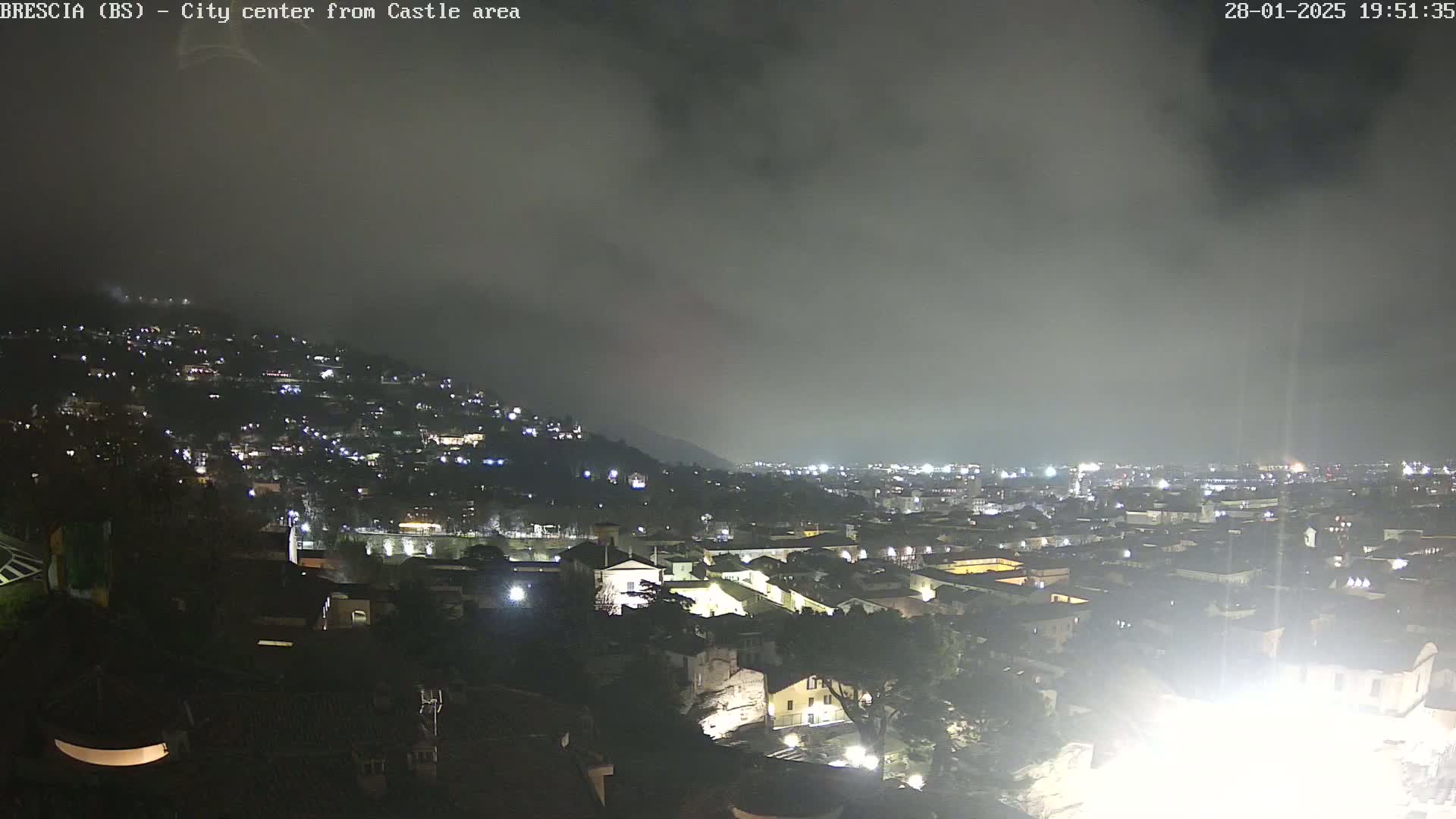 A nighttime view of a city sprawling across a hillside under a cloudy sky.