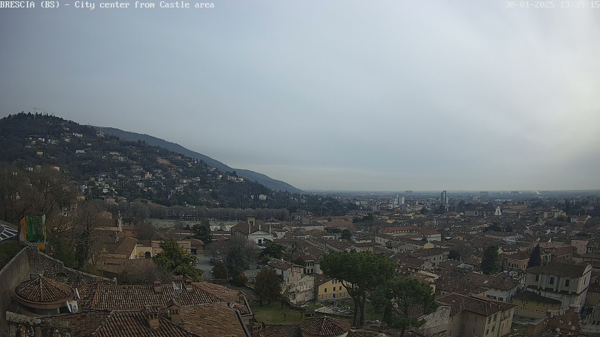 A sprawling city with red-tiled roofs nestled against a hillside under a hazy, overcast sky.