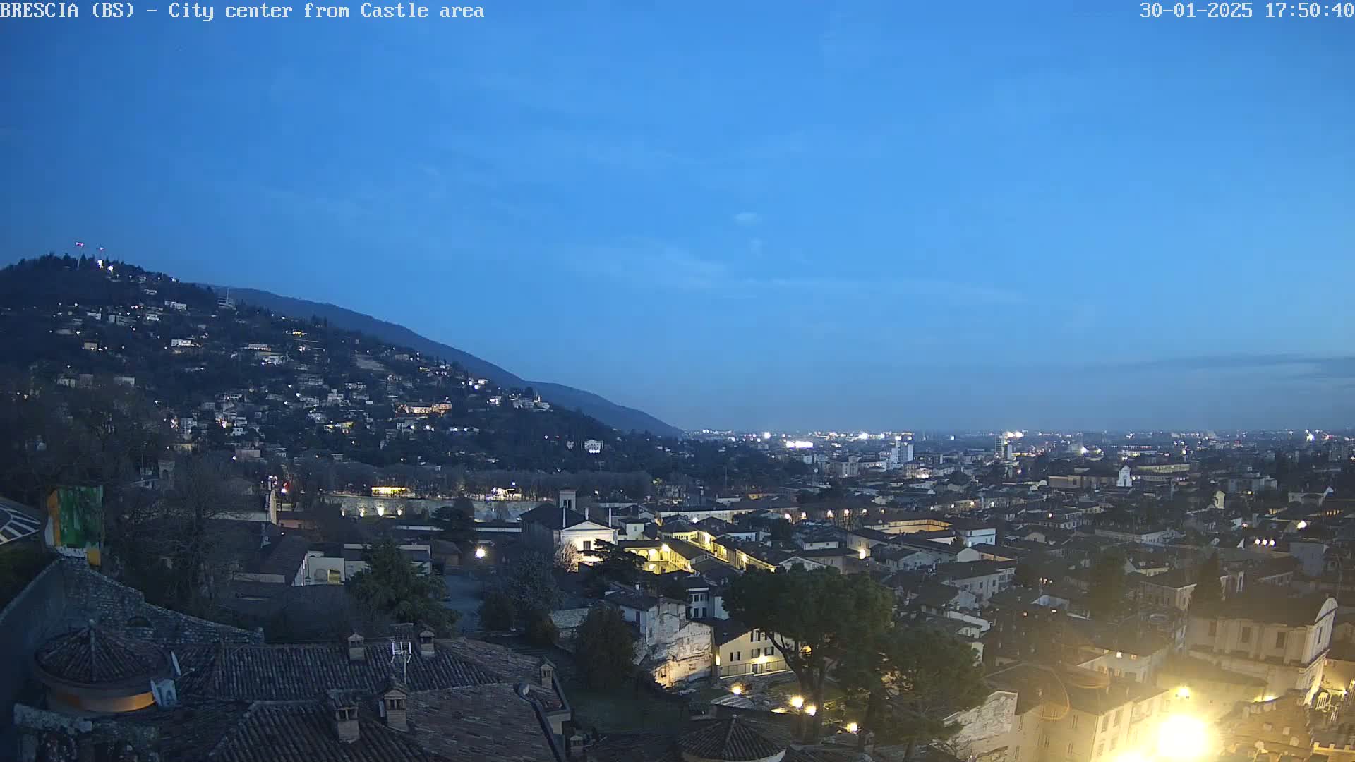 A nighttime view of a city nestled in a valley, illuminated by streetlights under a clear, twilight sky.