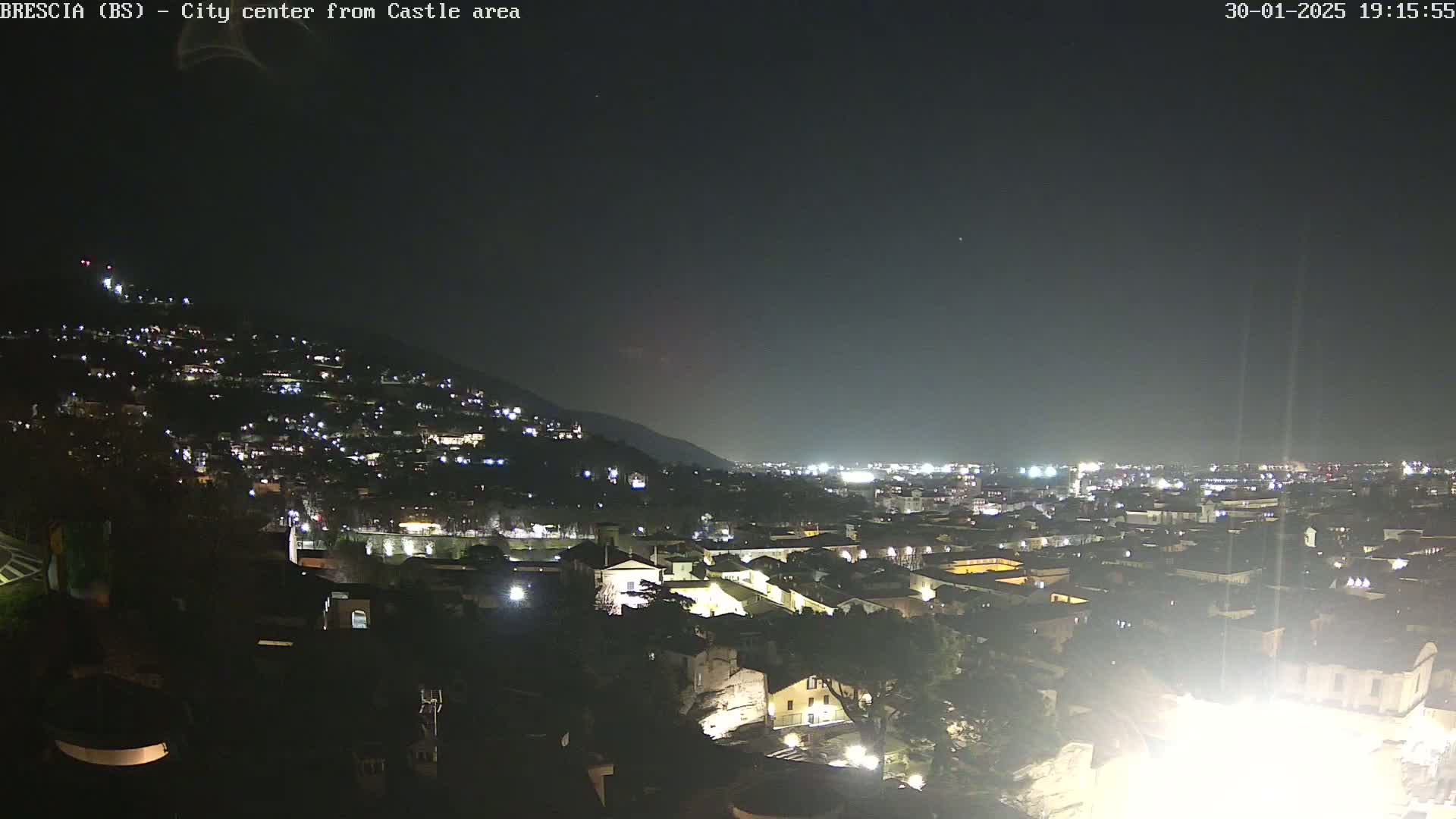 A nighttime, long shot of a city nestled against a hill, illuminated by numerous lights under a dark, clear sky.