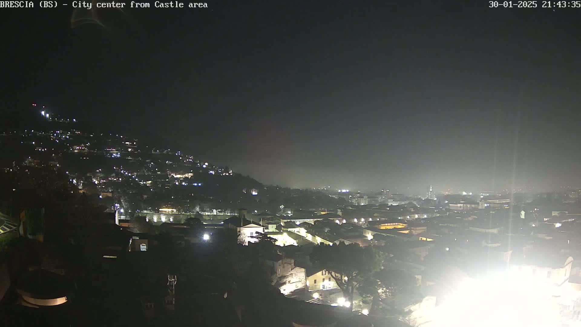 A nighttime, hazy view of a city spread across a hill, with many lights illuminating the buildings and streets.