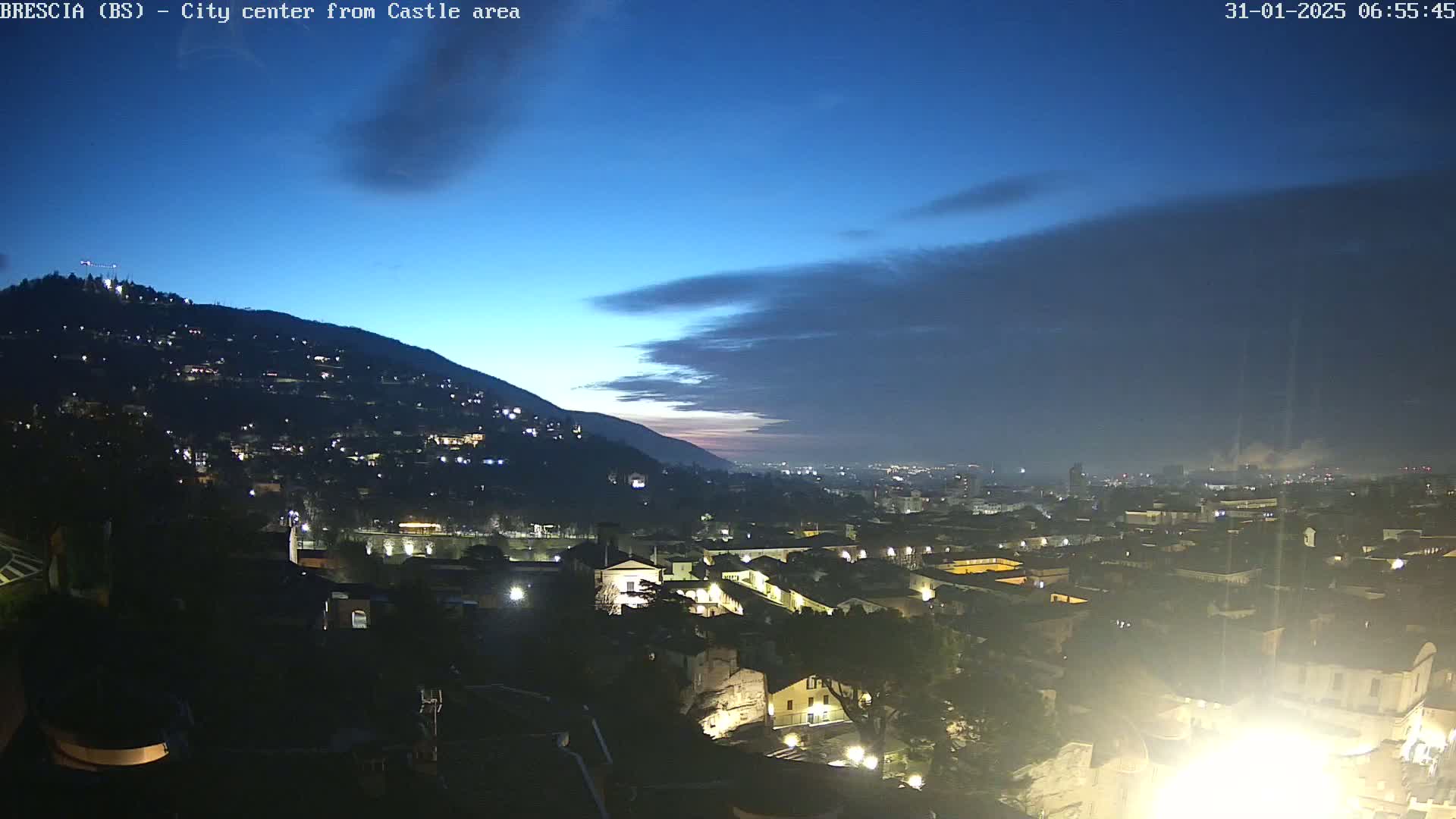 A nighttime view of a city nestled against a hill, under a twilight sky with some clouds.