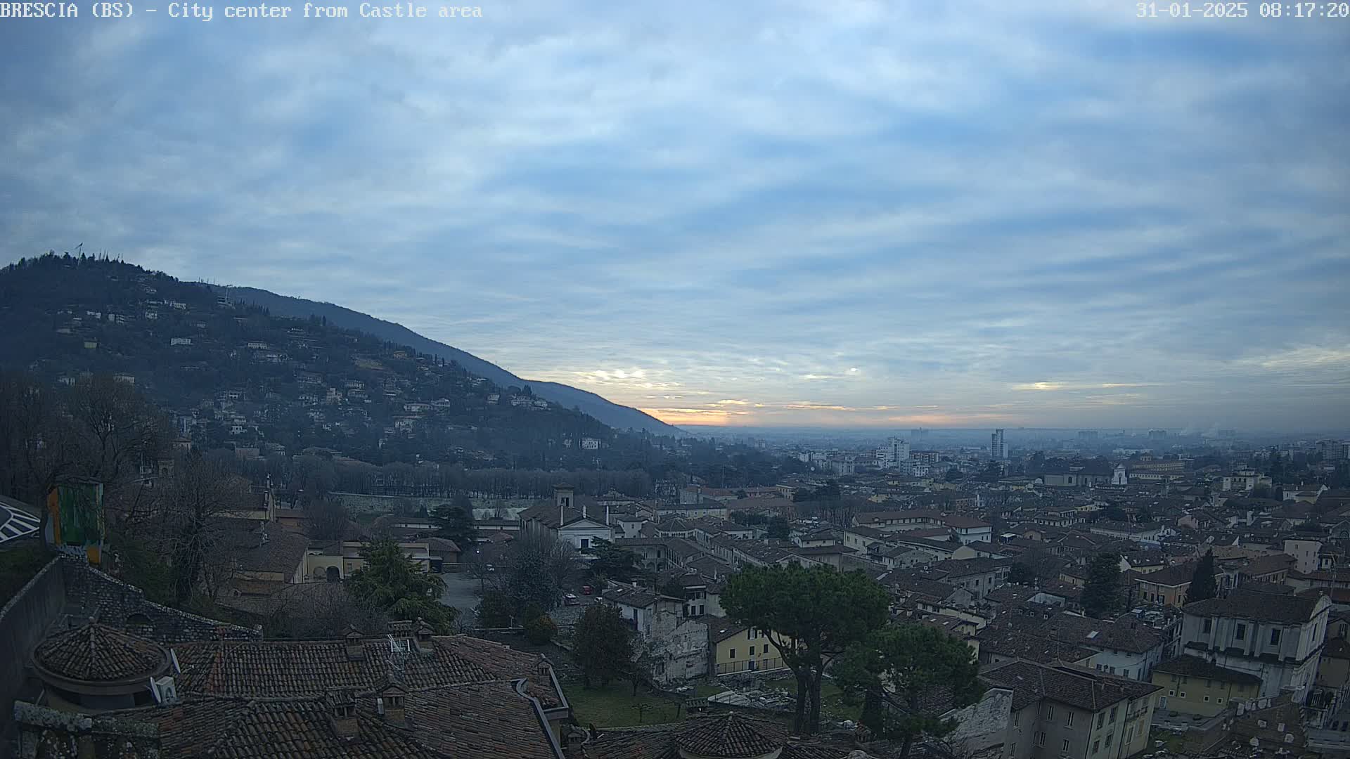 A sprawling city nestled in a valley between hills, under a mostly cloudy, dusky sky.