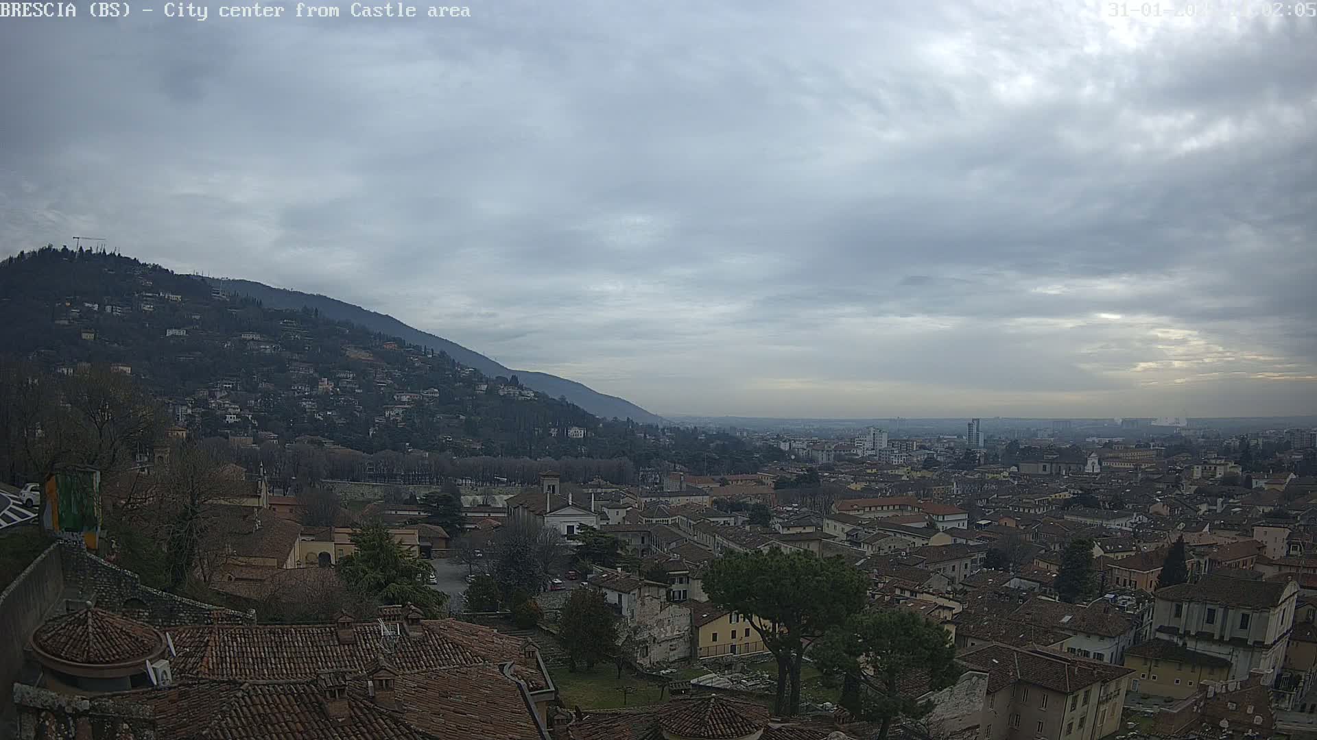 A cloudy day reveals a sprawling city nestled against a hillside, viewed from an elevated vantage point.