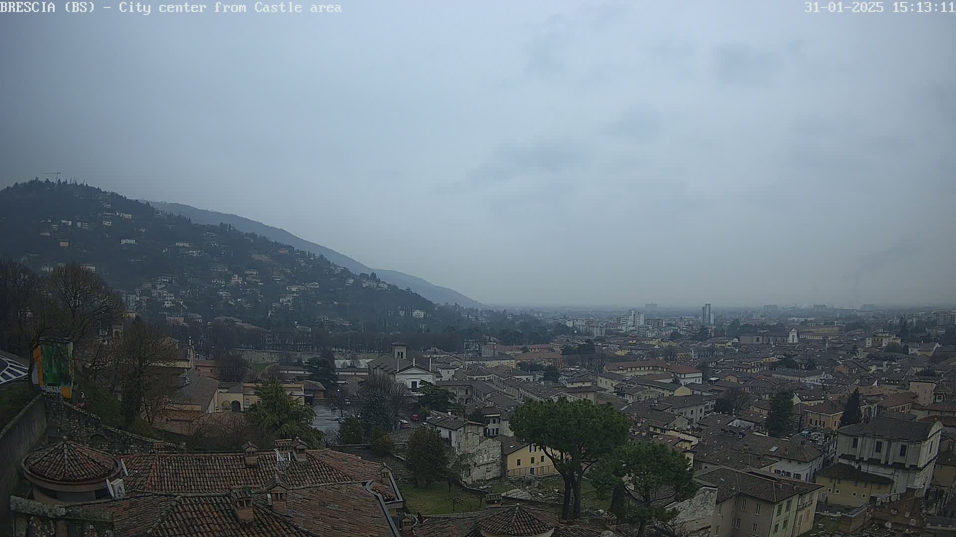 A hazy, overcast day reveals a sprawling city nestled in a valley between hills, viewed from a high vantage point.