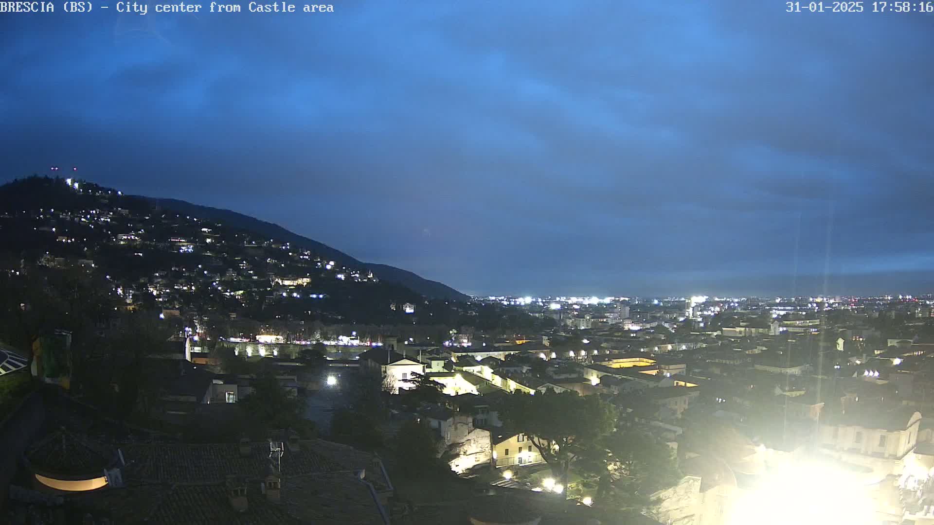 A nighttime view of a city nestled against a hill, under a mostly clear, twilight sky.