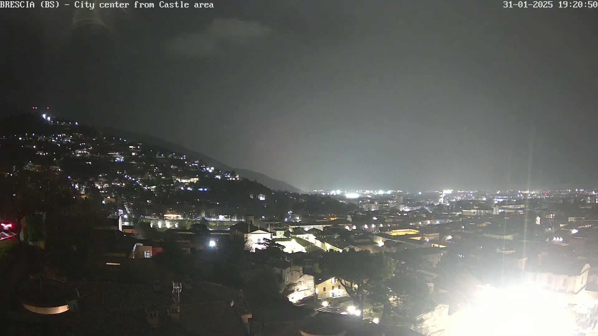 A nighttime view of a city nestled against a hillside under a dark, overcast sky.