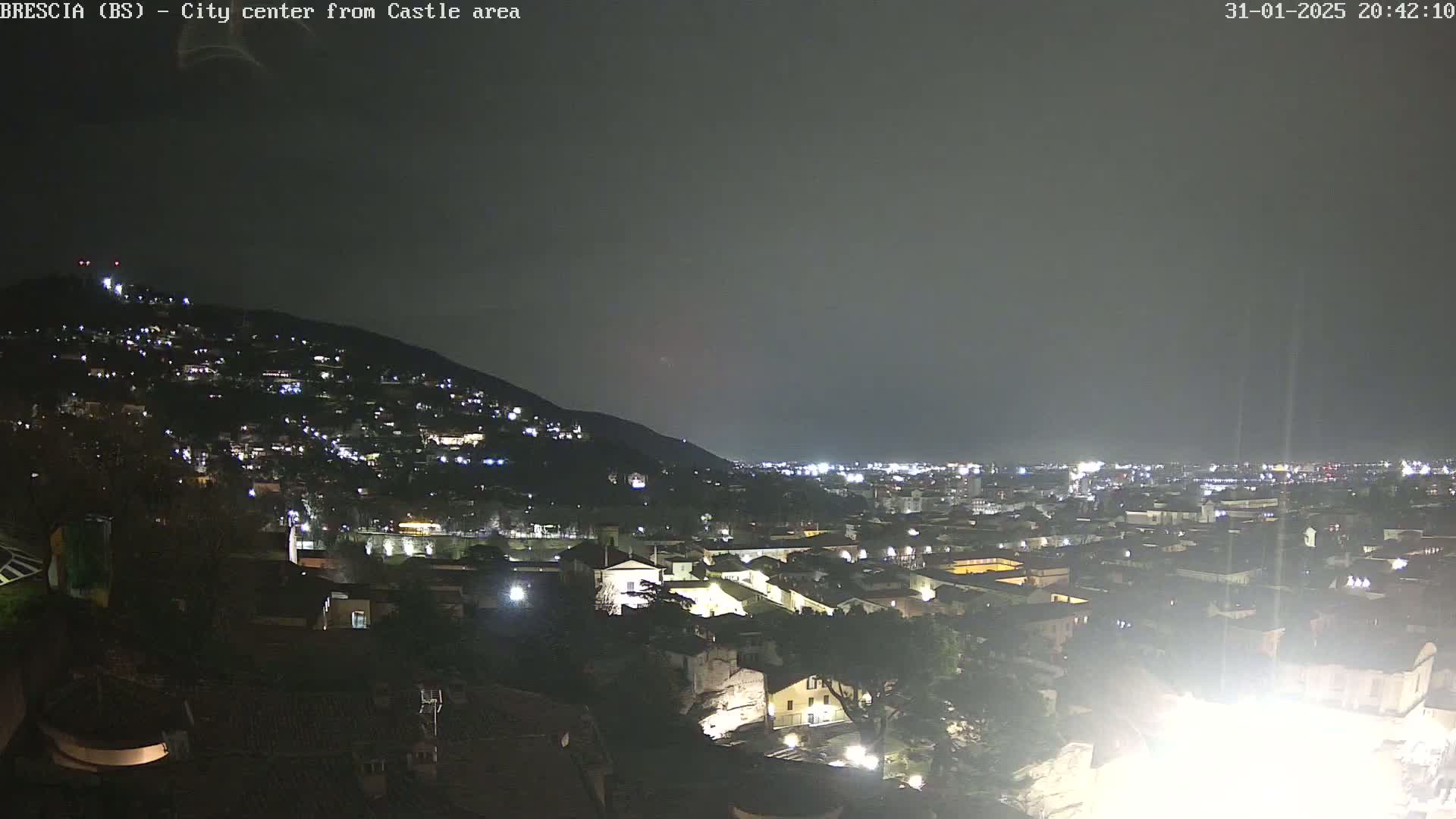 A nighttime view of a city sprawling across a hill and into a valley under a dark, cloudy sky.