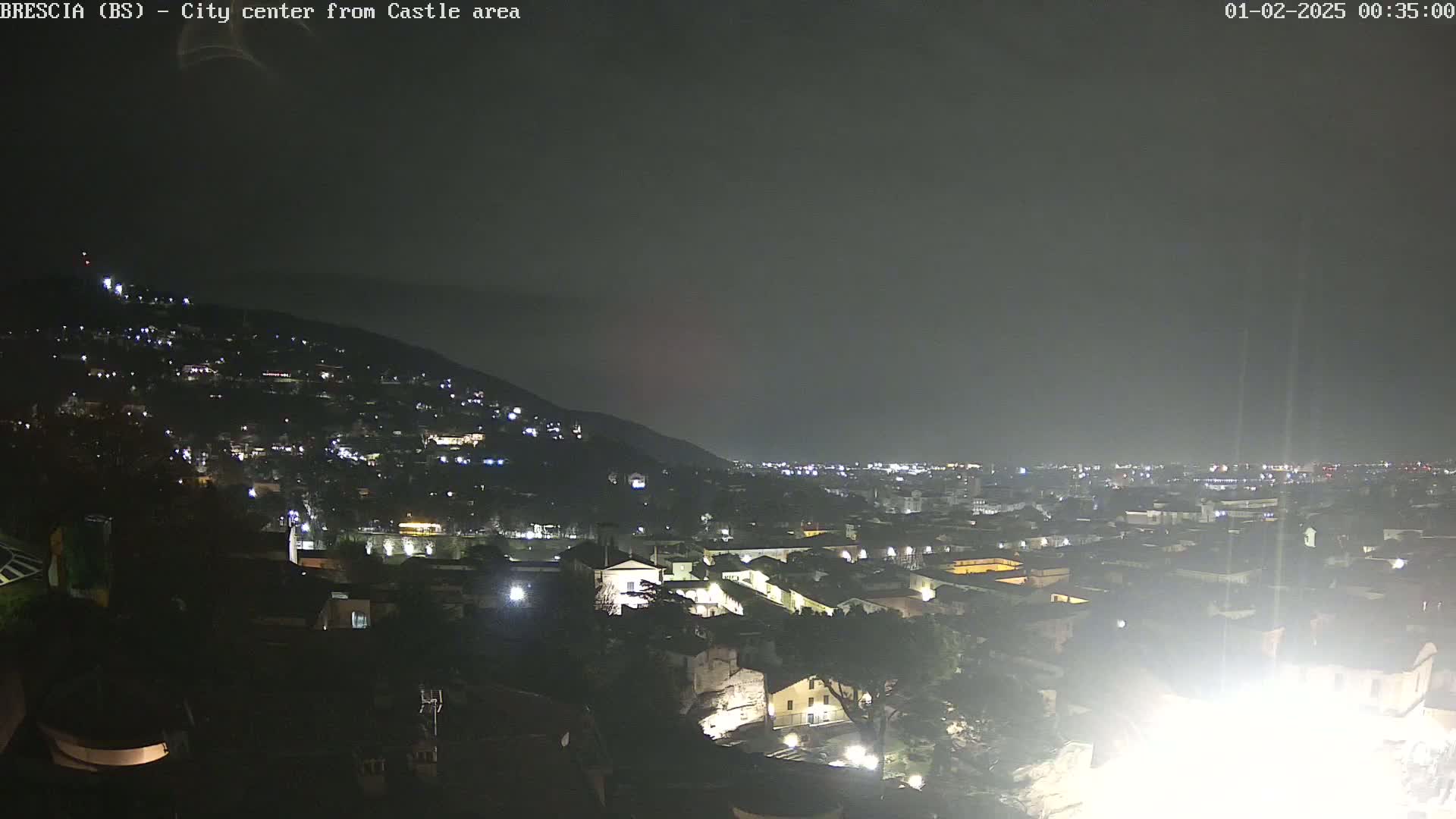 A nighttime view of a city nestled against a hill, under a dark, overcast sky.